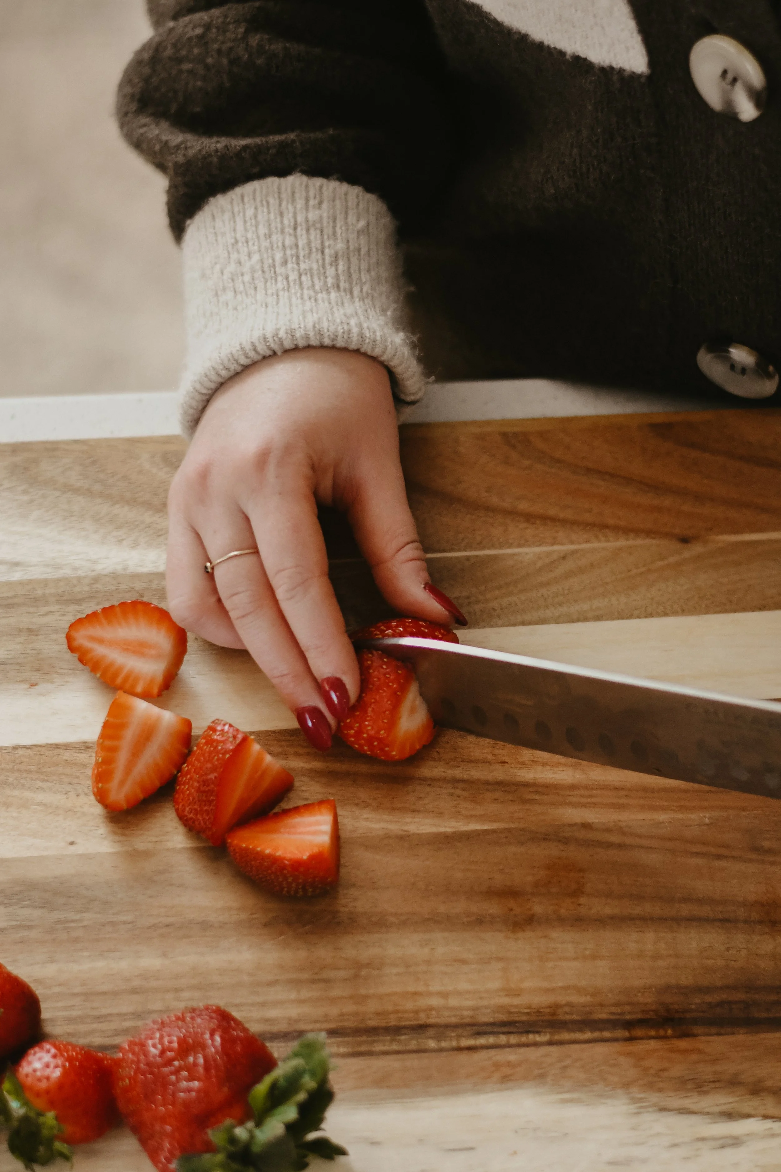 Person slicing strawberries on a wooden cutting board.