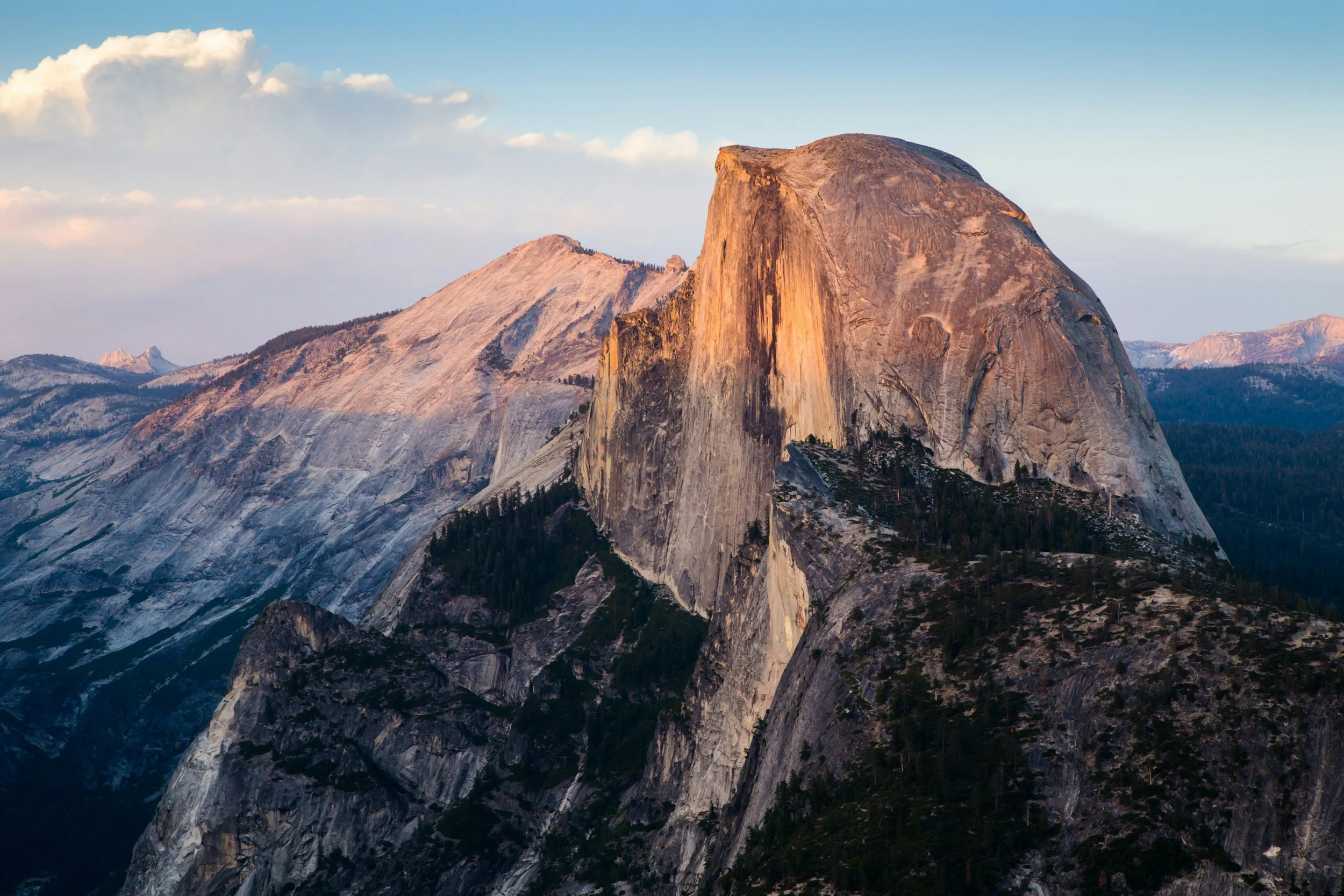 Mountains with a prominent dome-shaped rock formation, likely Half Dome in Yosemite National Park, during sunset or sunrise.