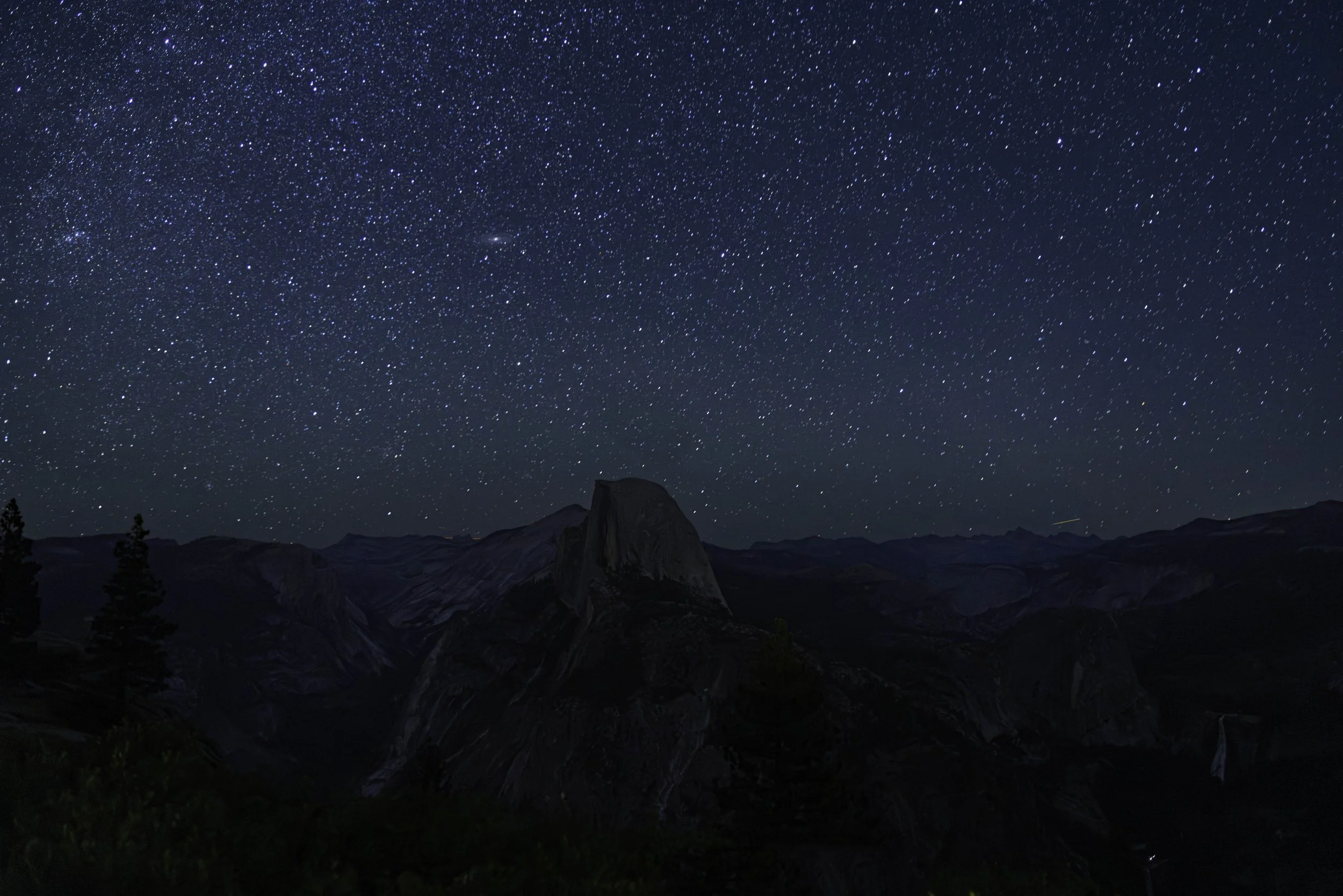 Night sky filled with stars over a mountain landscape with distinctive rock formations.