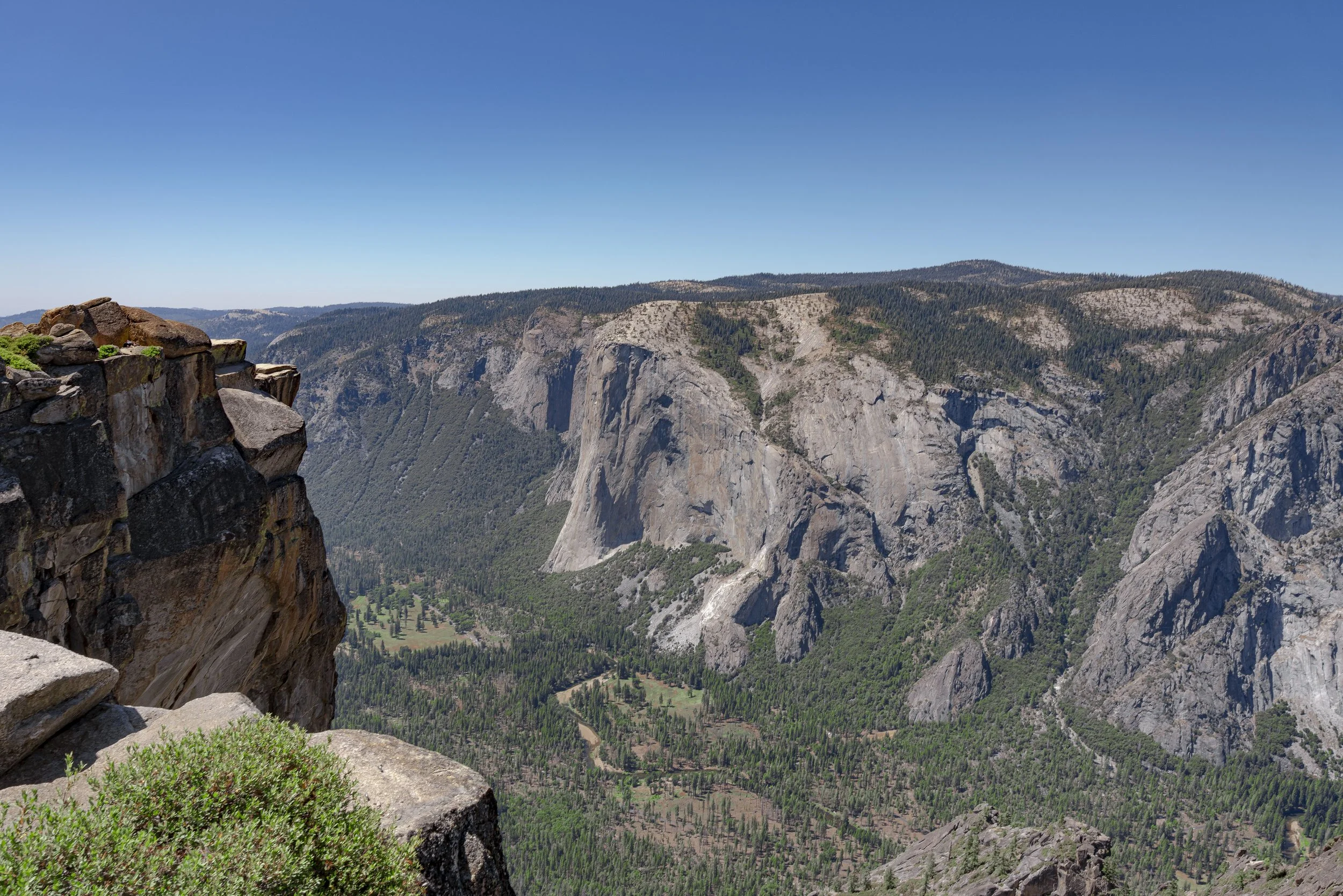 Scenic view of Yosemite Valley with granite cliffs, lush green forest, and clear blue sky.