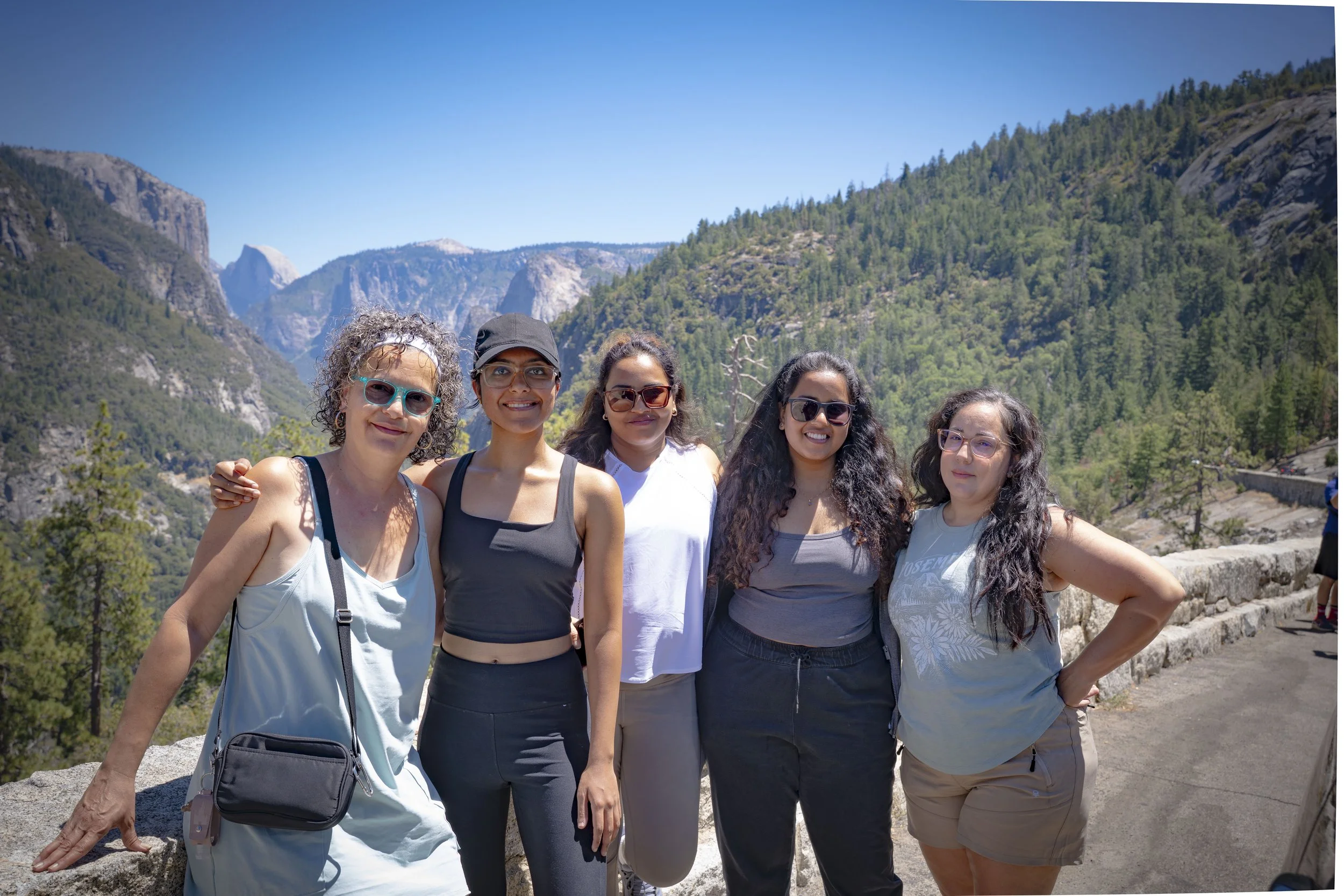 Group of five women posing together outdoors with mountainous landscape in the background.