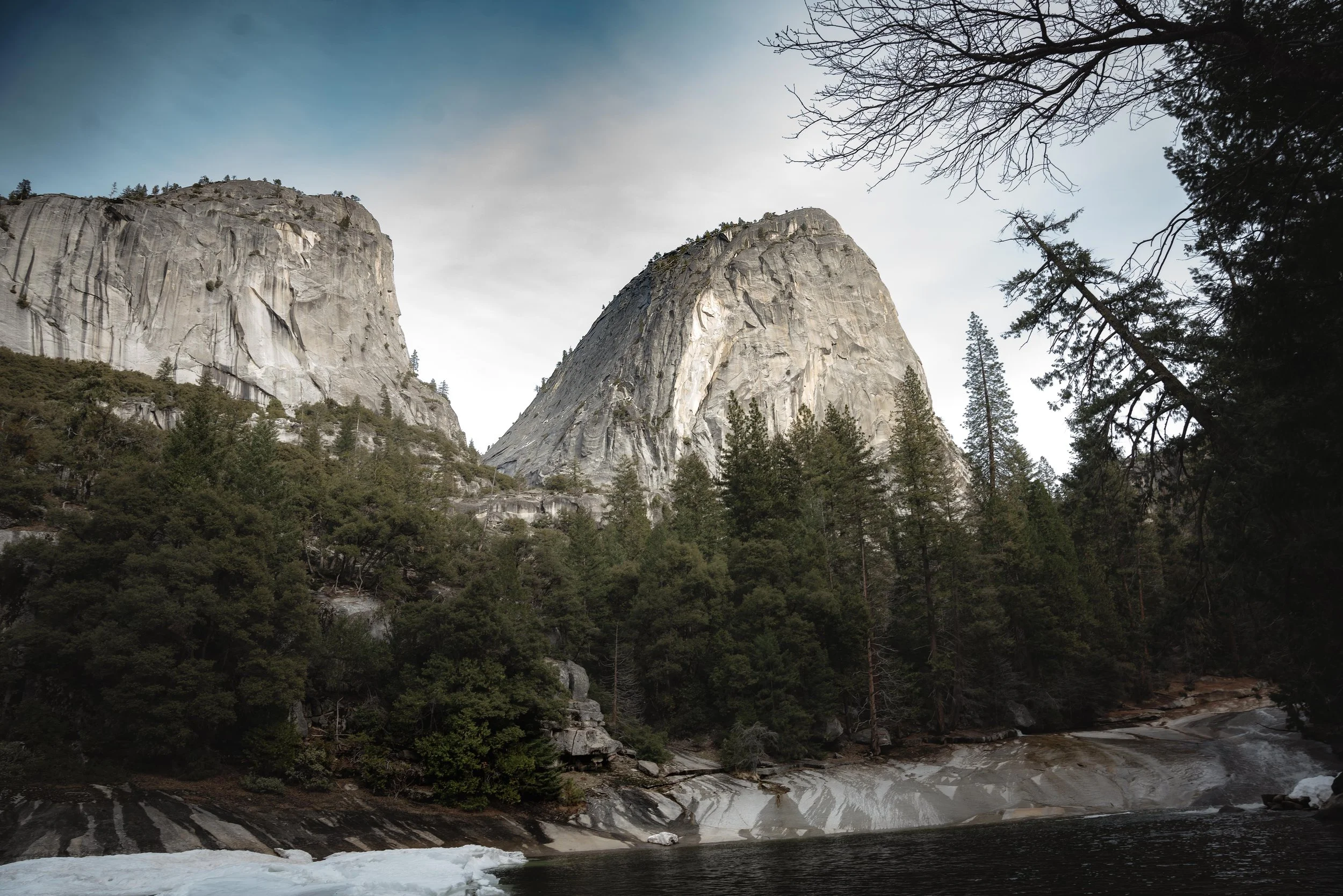A view of a mountain landscape with large granite cliffs, a forested area, and a river in the foreground.