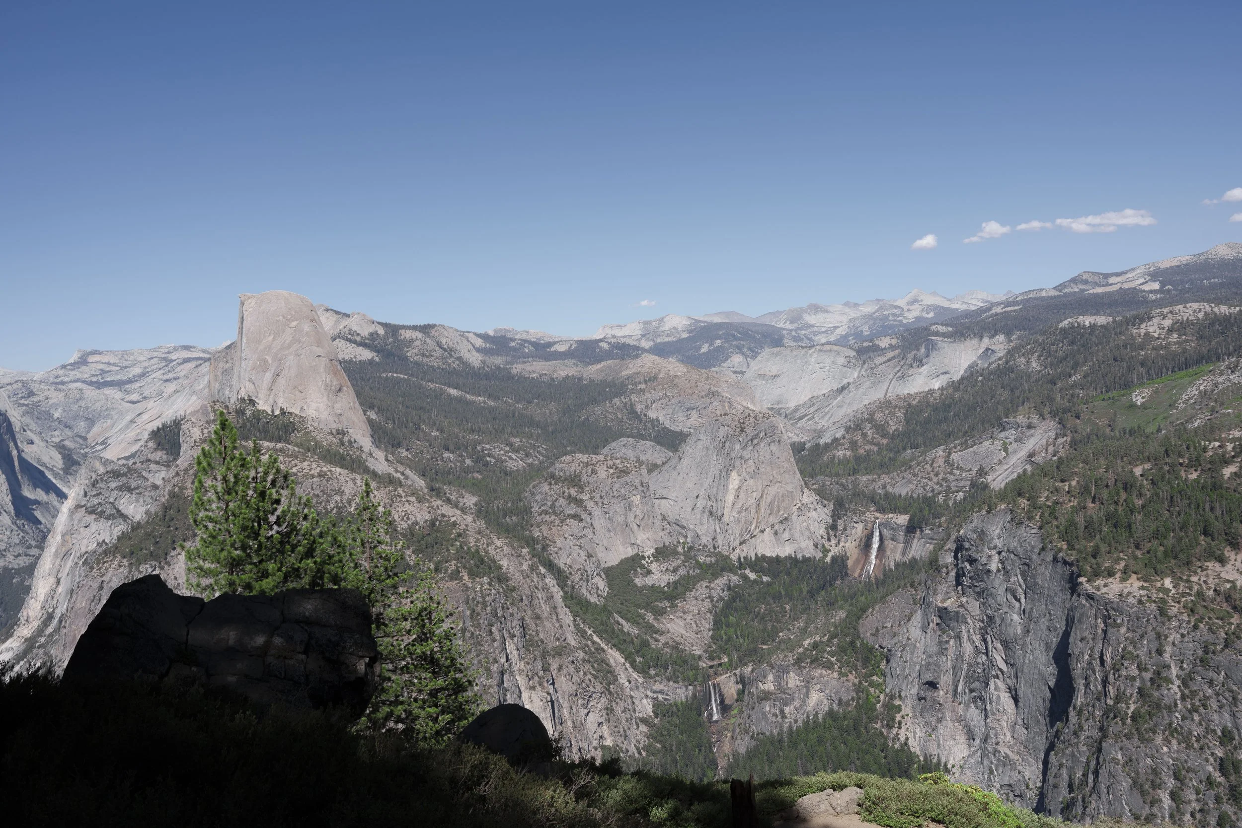 Scenic view of mountains with rocks, trees, and waterfalls under a blue sky.