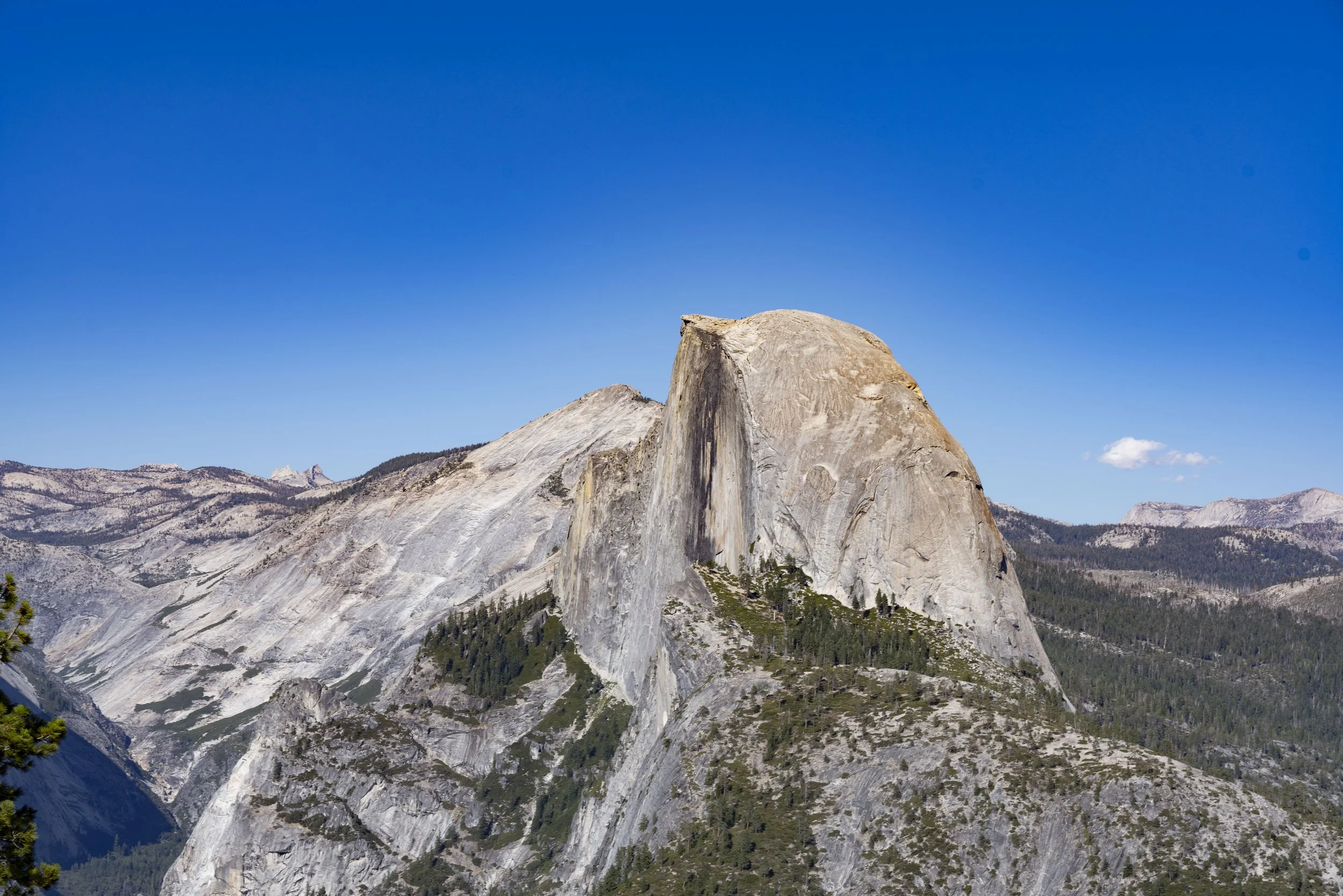 Large granite rock formation in a mountainous landscape under a clear blue sky.