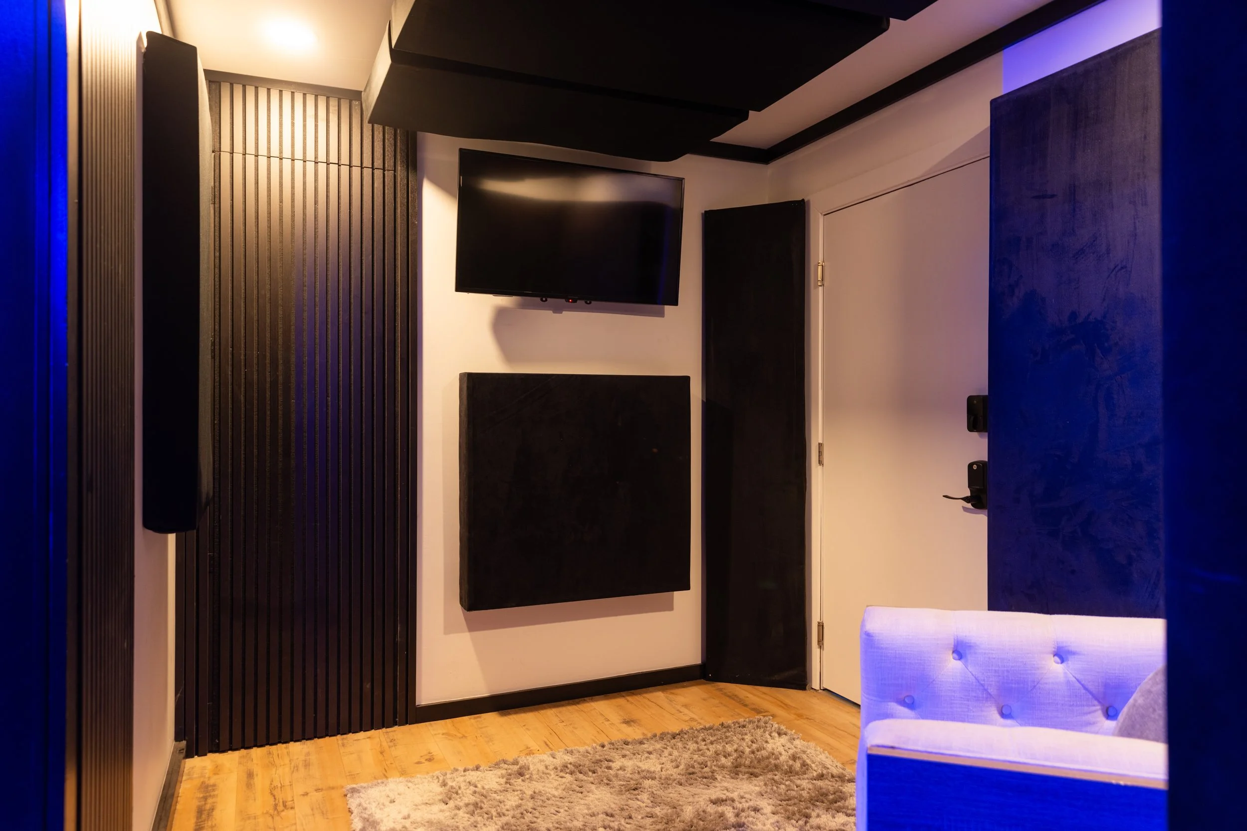 Modern soundproof room with acoustic panels, a mounted TV, and a plush rug on wooden flooring.