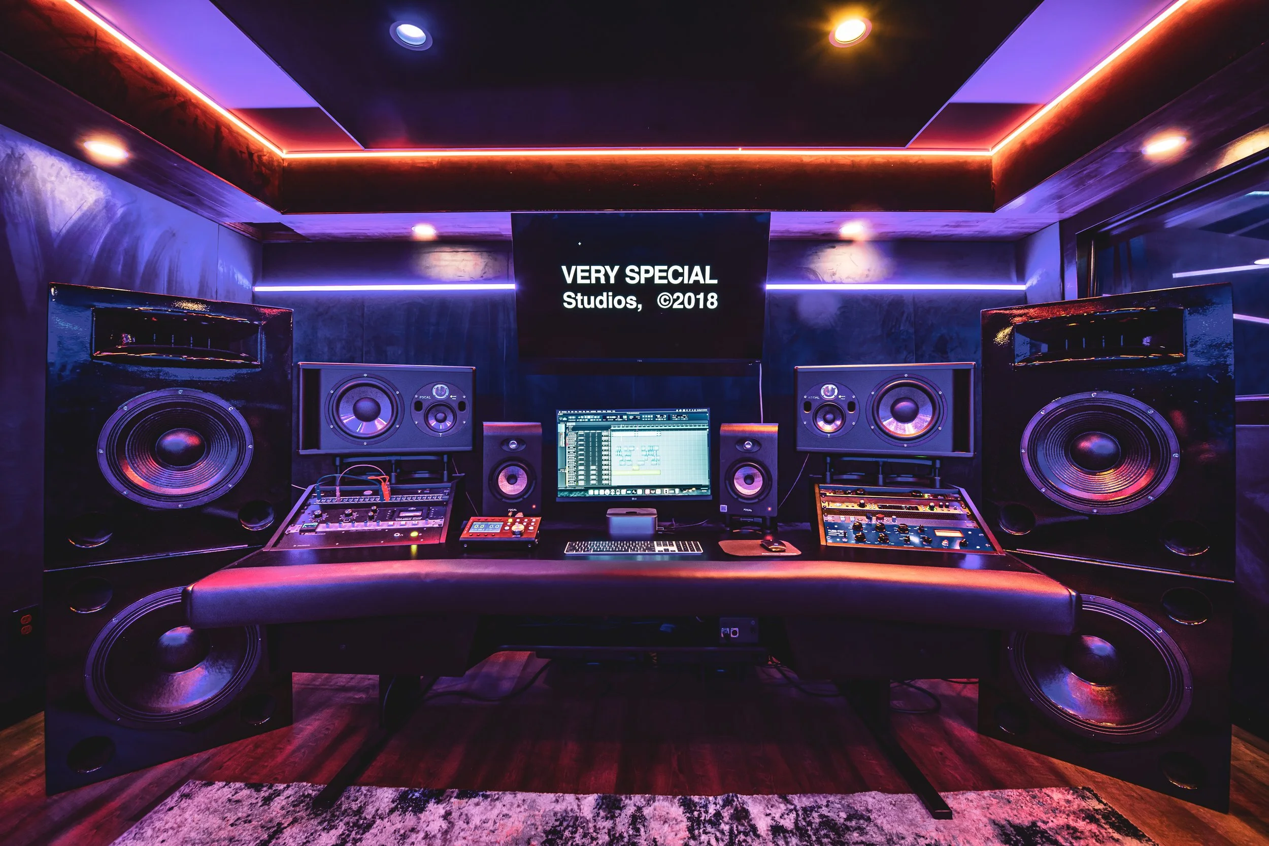 Modern music studio setup with large speakers, monitor screen, audio equipment, and ambient lighting.