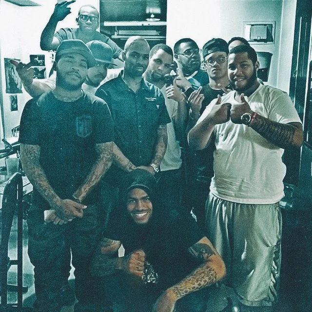 Group of men posing together indoors, some displaying hand gestures, in casual clothing.