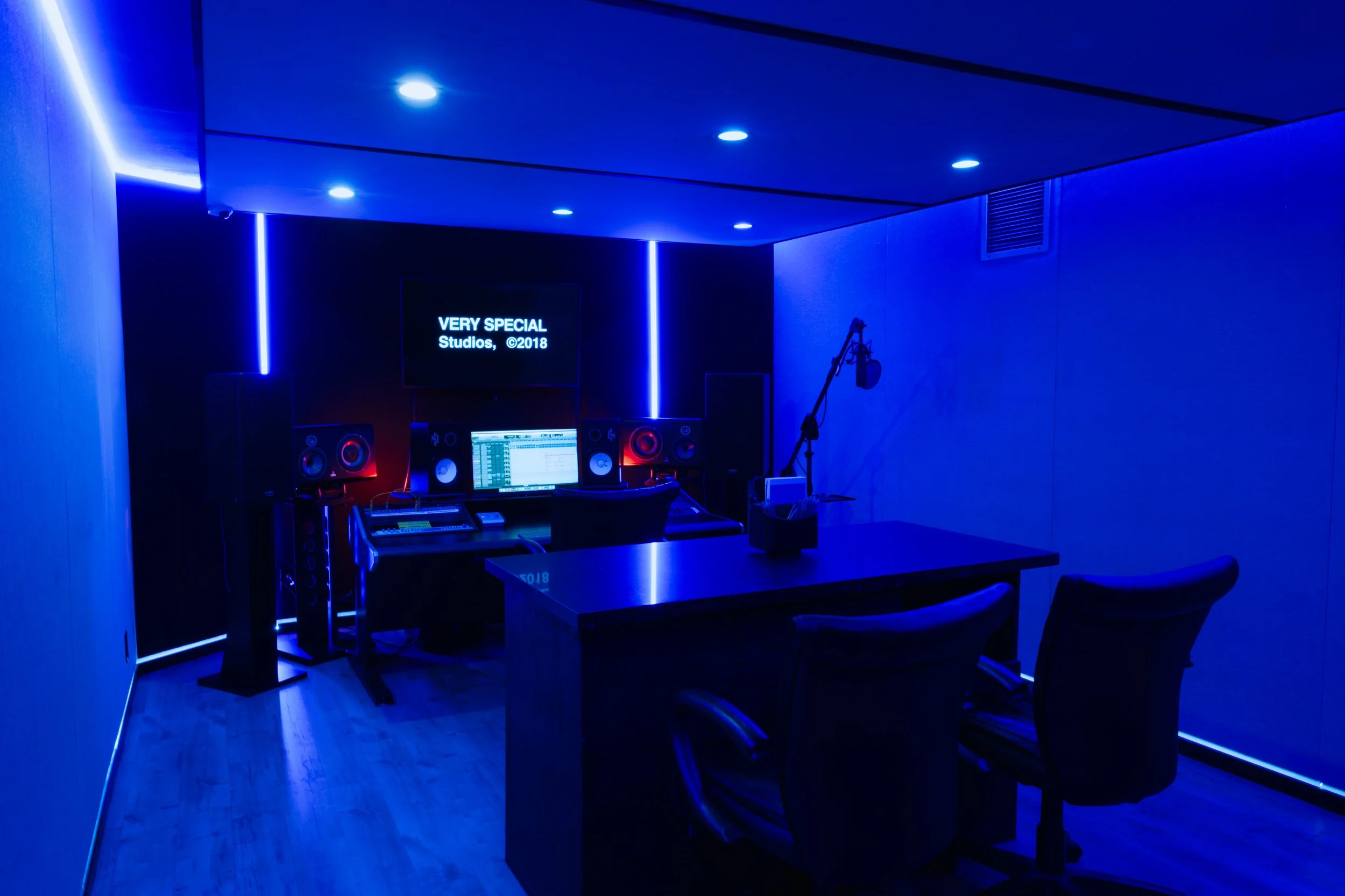 Modern recording studio with blue lighting, computer monitor, large speakers, and microphone
