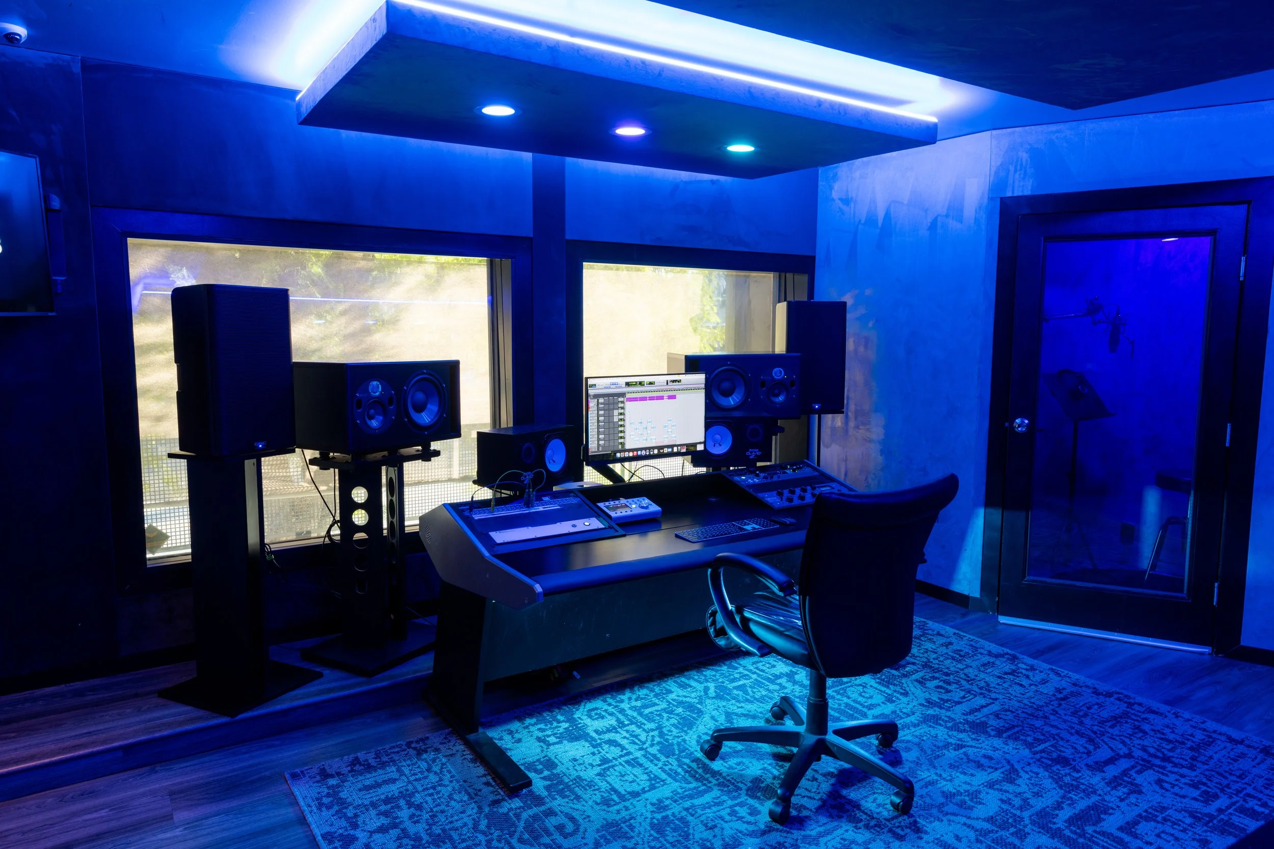 Professional music recording studio with mixing console, speakers, and computer monitor, blue ambient lighting