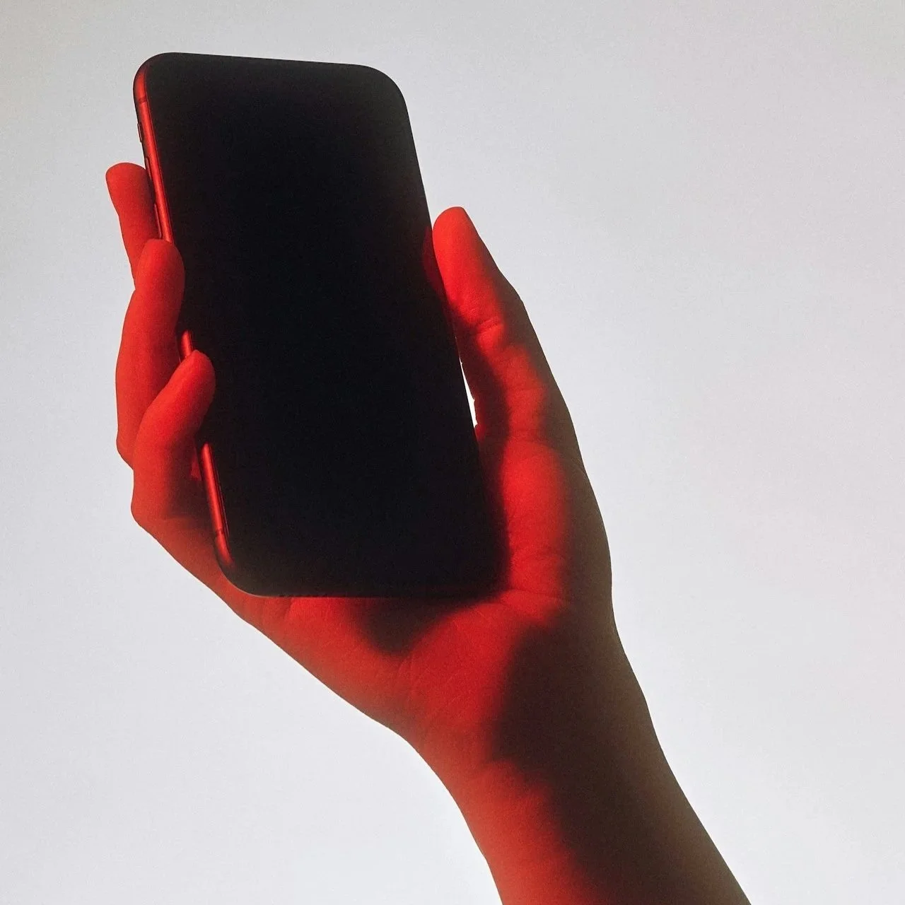 A human hand holding a smartphone with a black screen against a plain background.