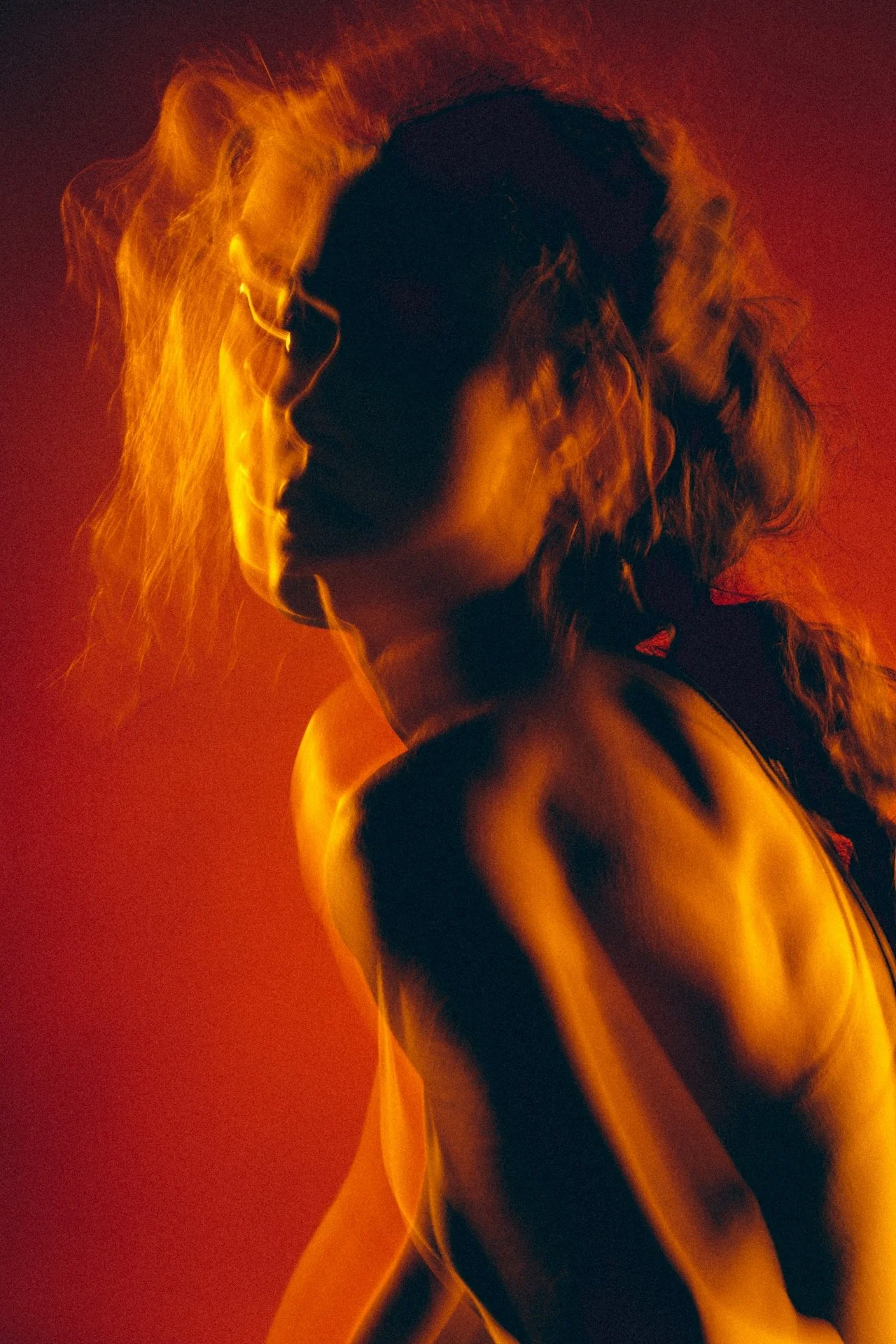 A silhouette of a woman with curly hair illuminated by warm orange and red lighting, creating a dramatic and artistic effect.