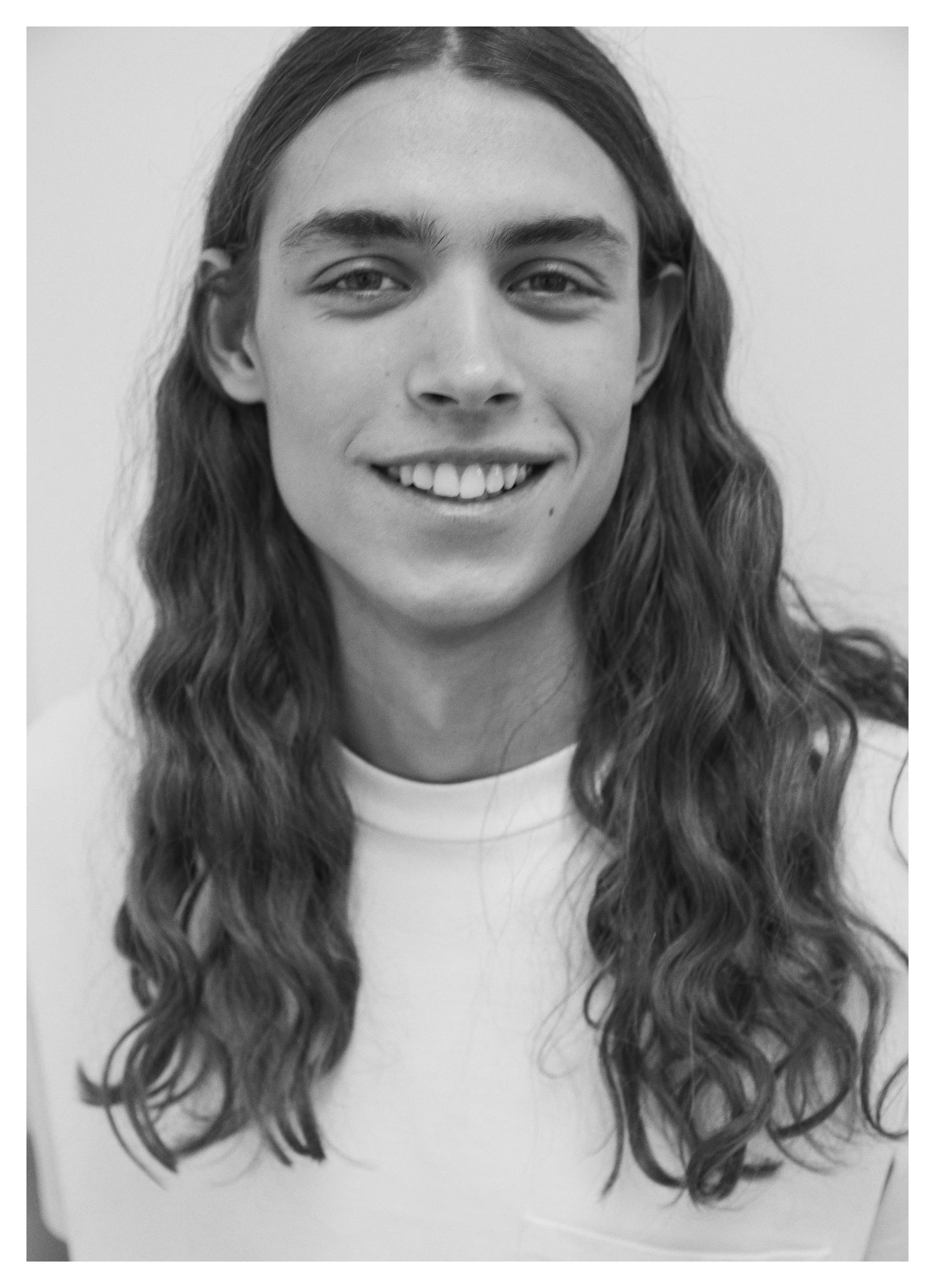 Portrait d'une jeune femme avec des cheveux longs ondulés et un sourire, en noir et blanc.