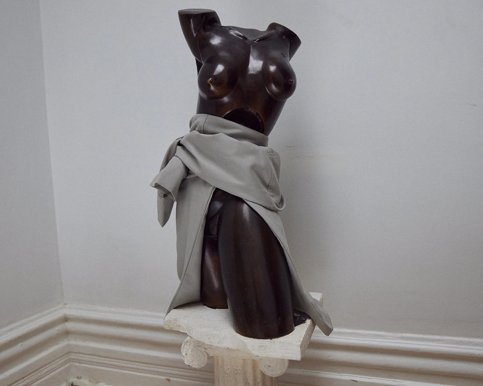 Une sculpture en bois d'une silhouette féminine portant un vêtement beige, exposée dans un espace intérieur.