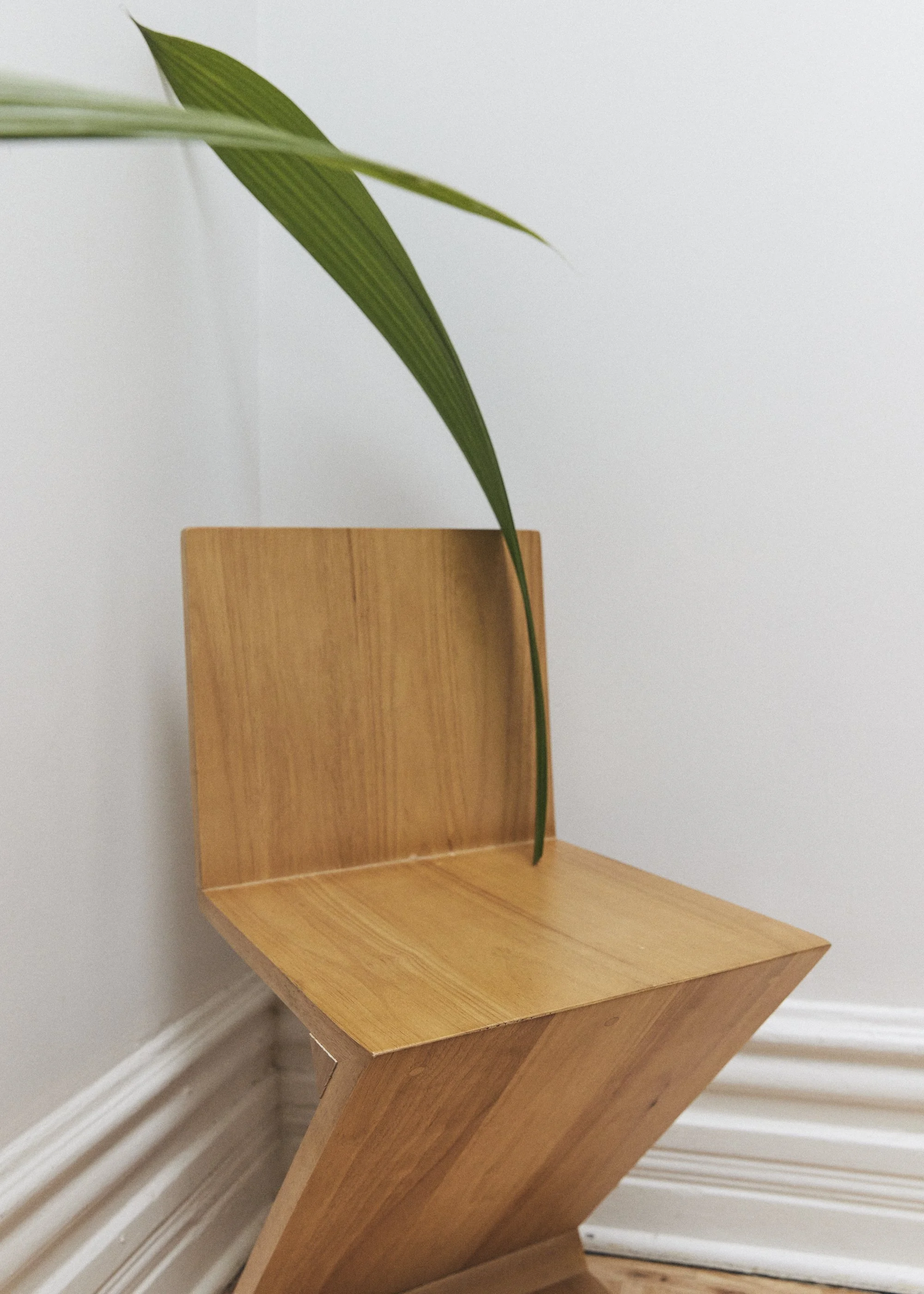 Une chaise en bois au design moderne, placée dans un coin d'une pièce avec un mur blanc et une plinthe blanche.