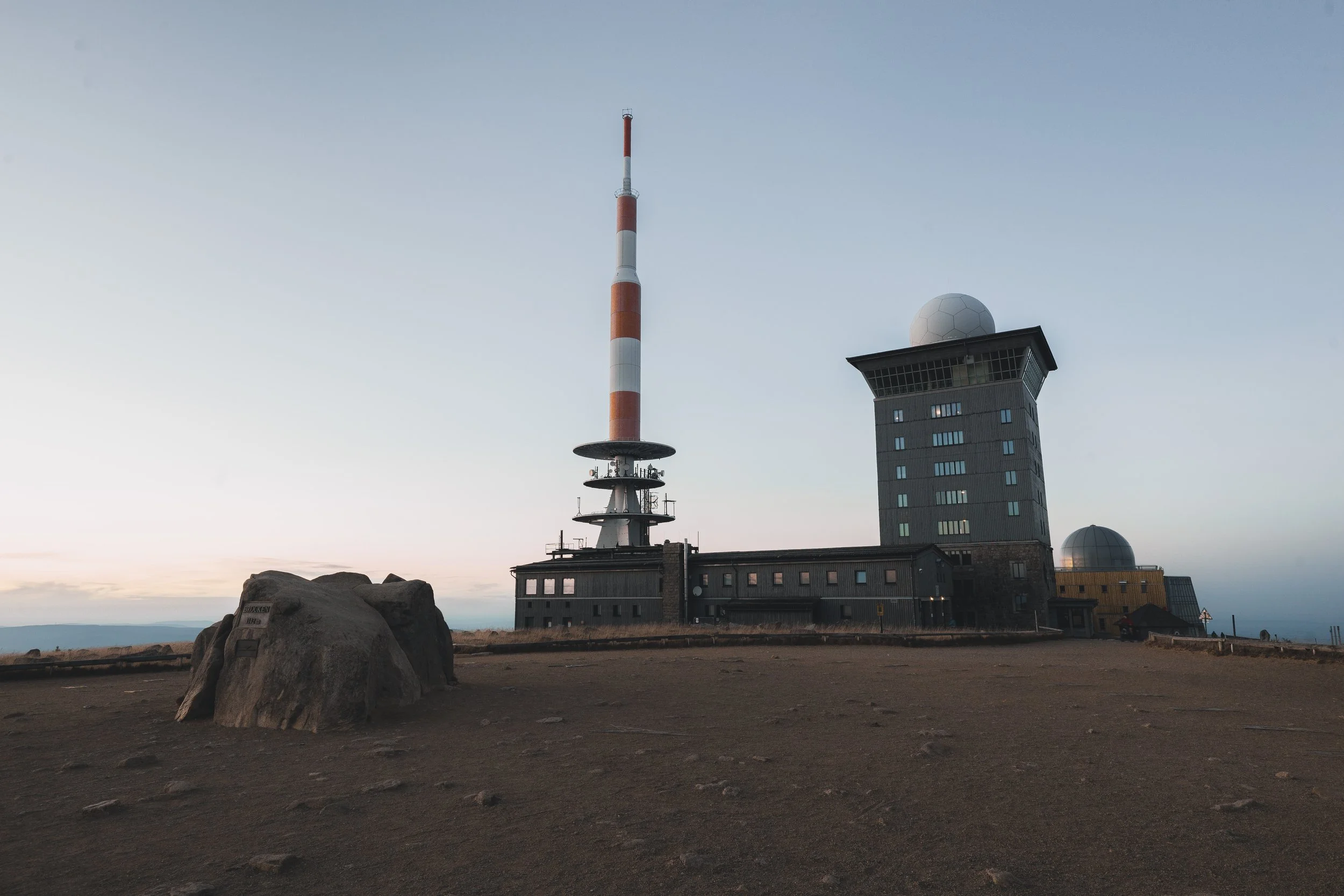 Ein Telekommunikationsturm und ein Wetterobservatorium auf einer Bergkuppe bei Sonnenuntergang oder Dämmerung.