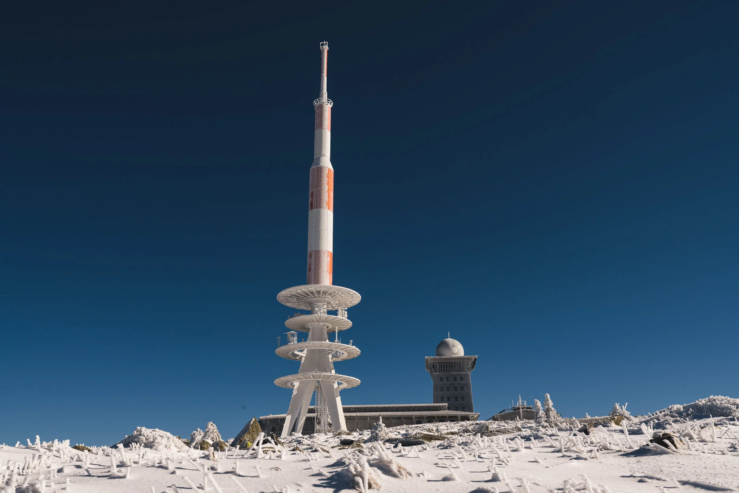 Sendeantenne und Gebäude auf verschneitem Gipfel unter klarem blauen Himmel