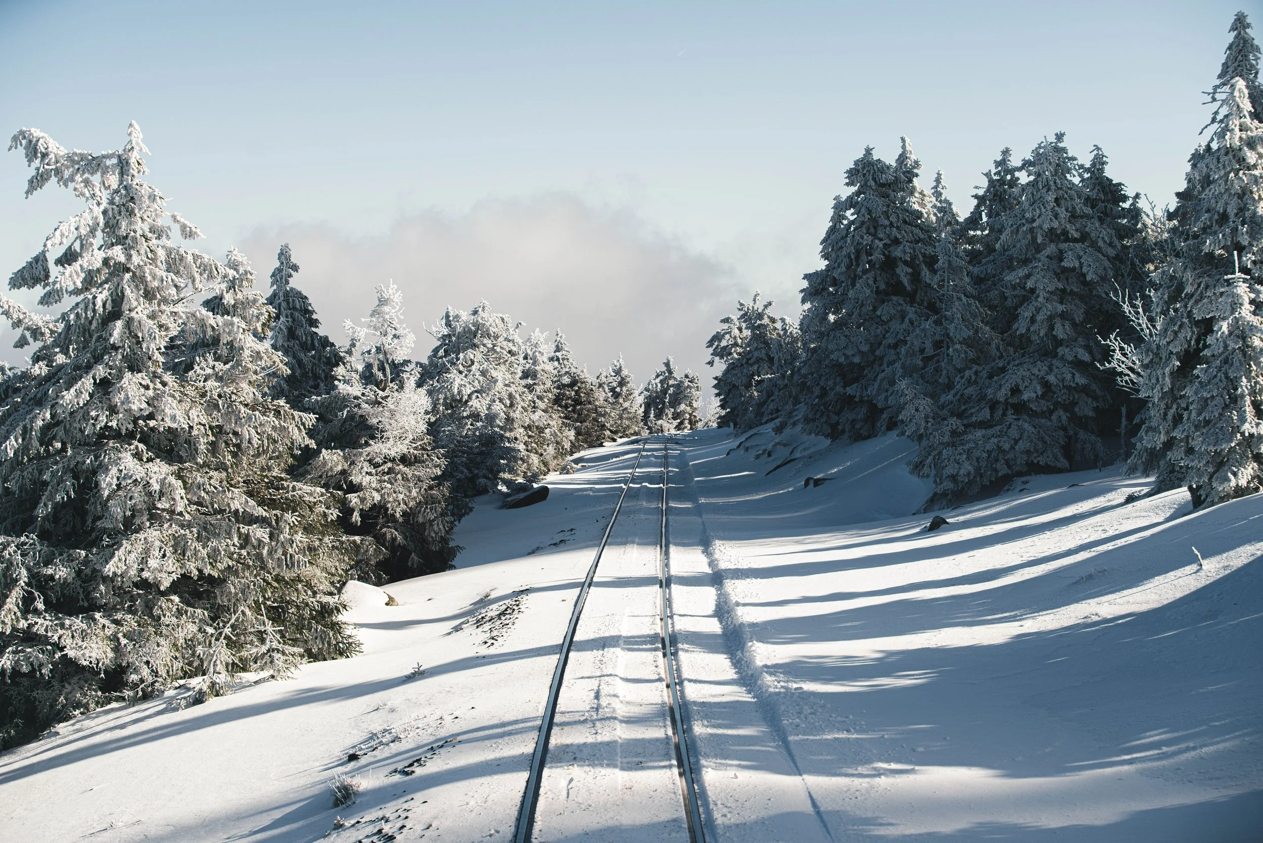 Schmaler Eisenbahn- oder Bahngleise verlaufen durch verschneiten Wald mit Schneebedeckten Tannen, unter klarem blauen Himmel.