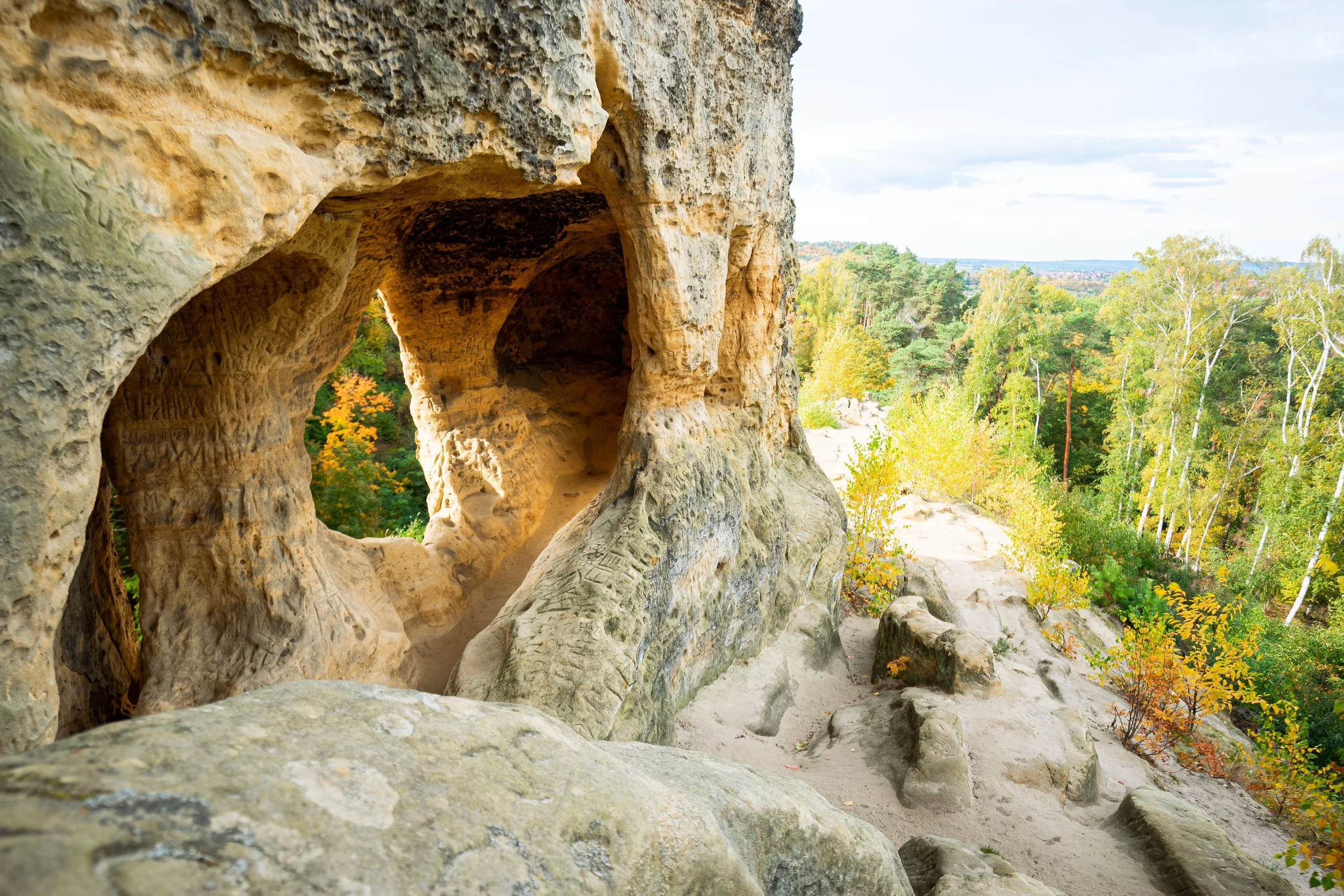 Felsformation mit Höhle und Blick auf einen Herbstwald mit grünen und gelben Bäumen
