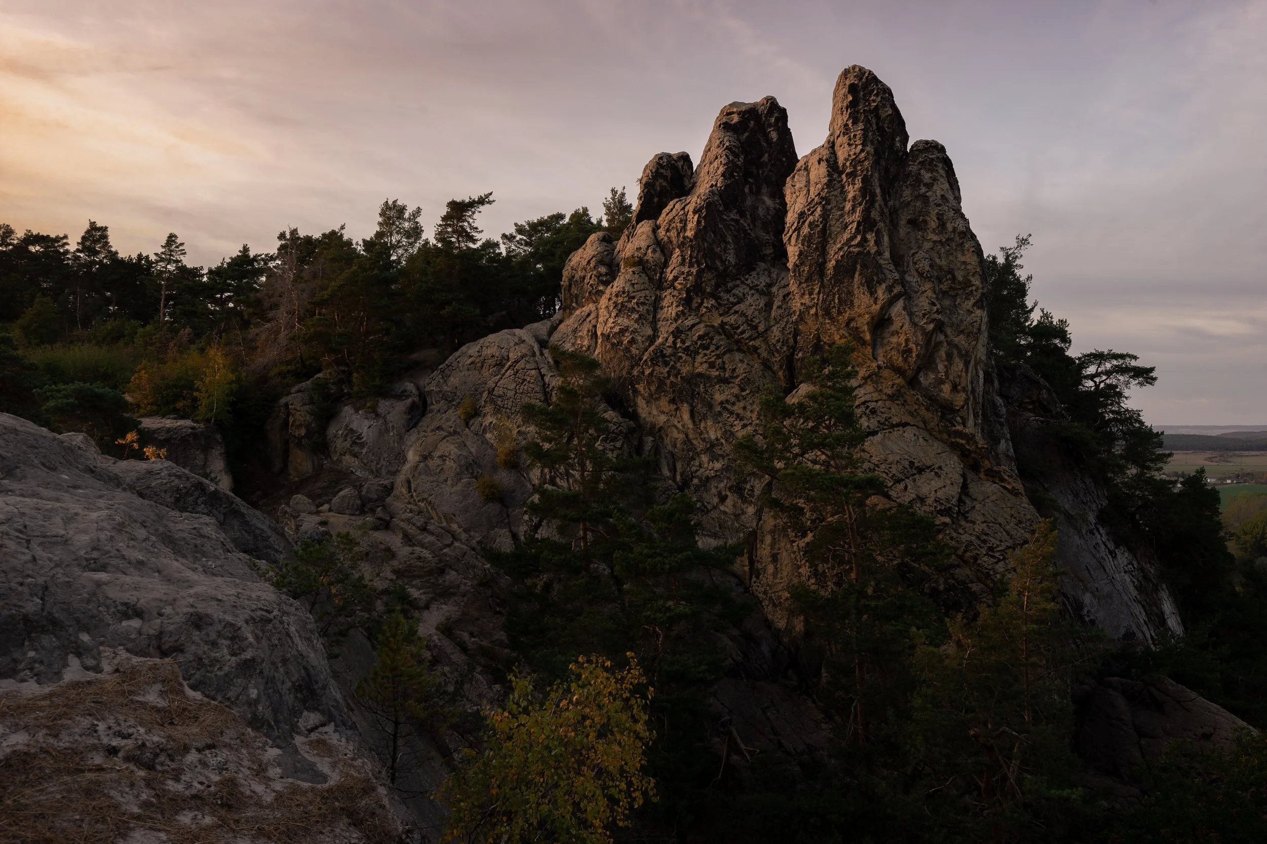 Felsen und Bäume in einer bewaldeten Hügellandschaft bei Sonnenuntergang.