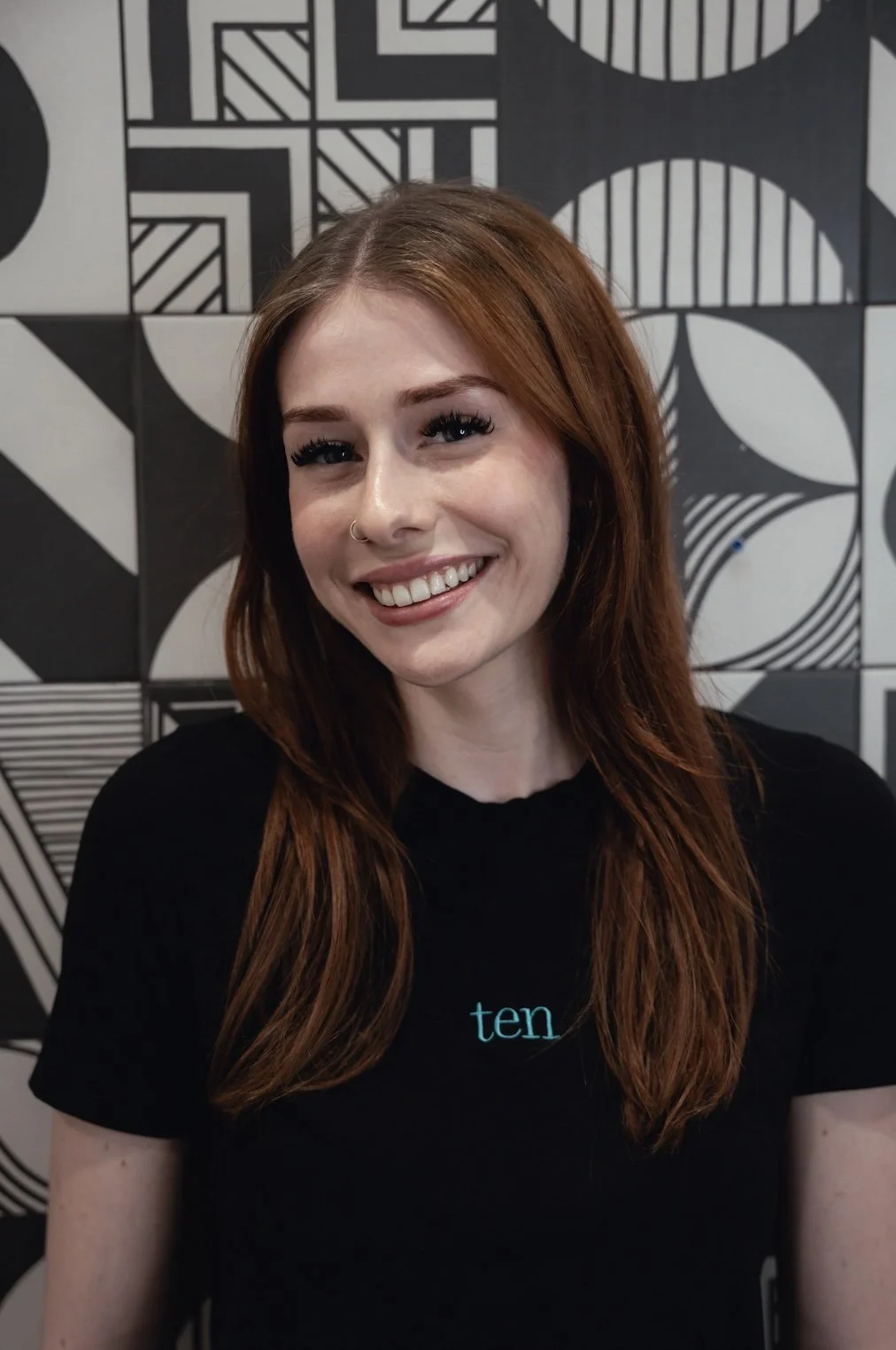 Smiling person wearing a green shirt with a white brick wall background.