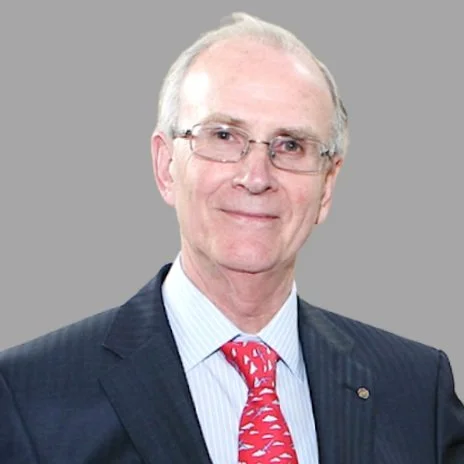 A person wearing glasses and a suit with a red tie, smiling against a gray background.