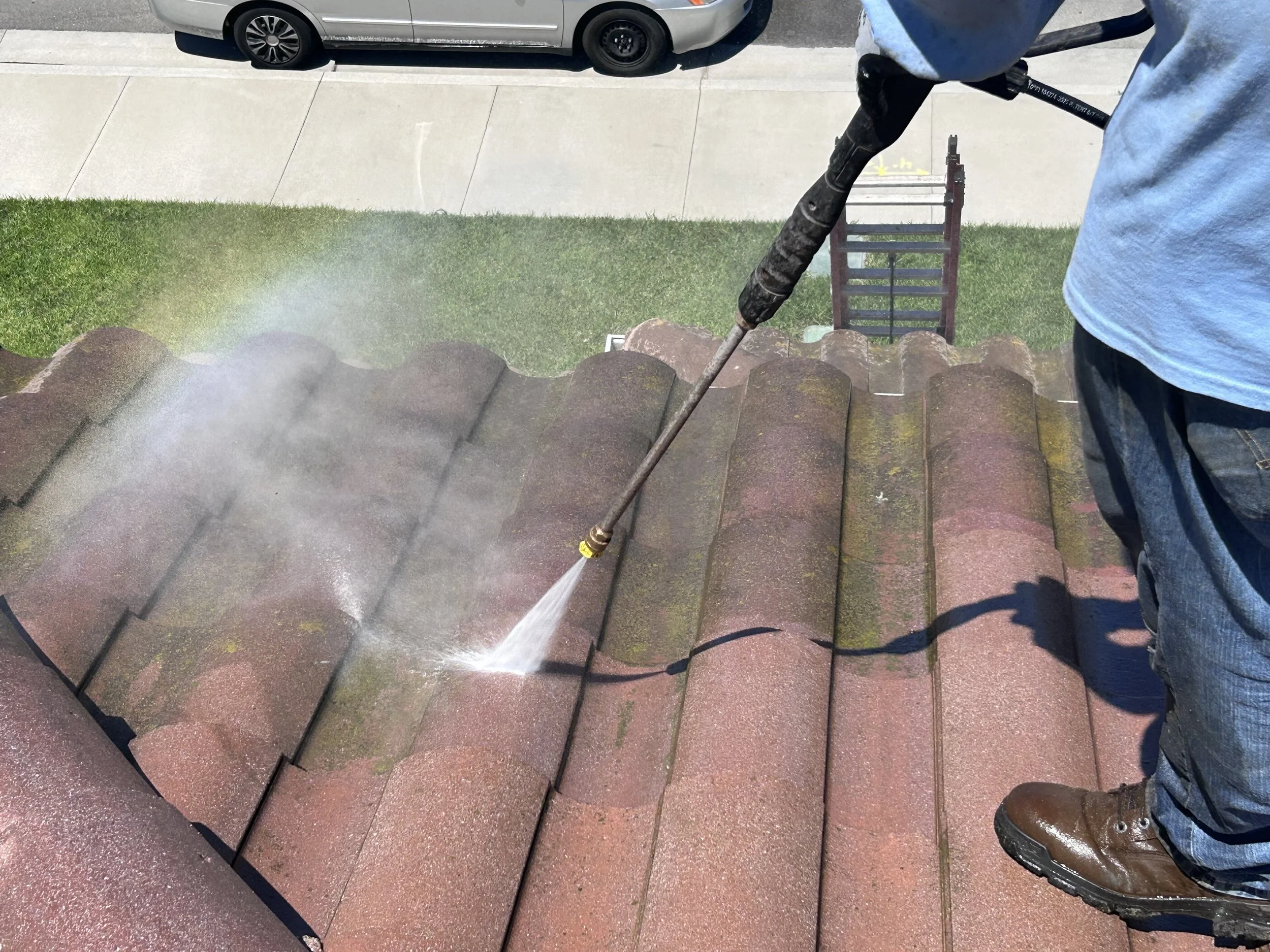 Person using a pressure washer to clean clay tile roof shingles.