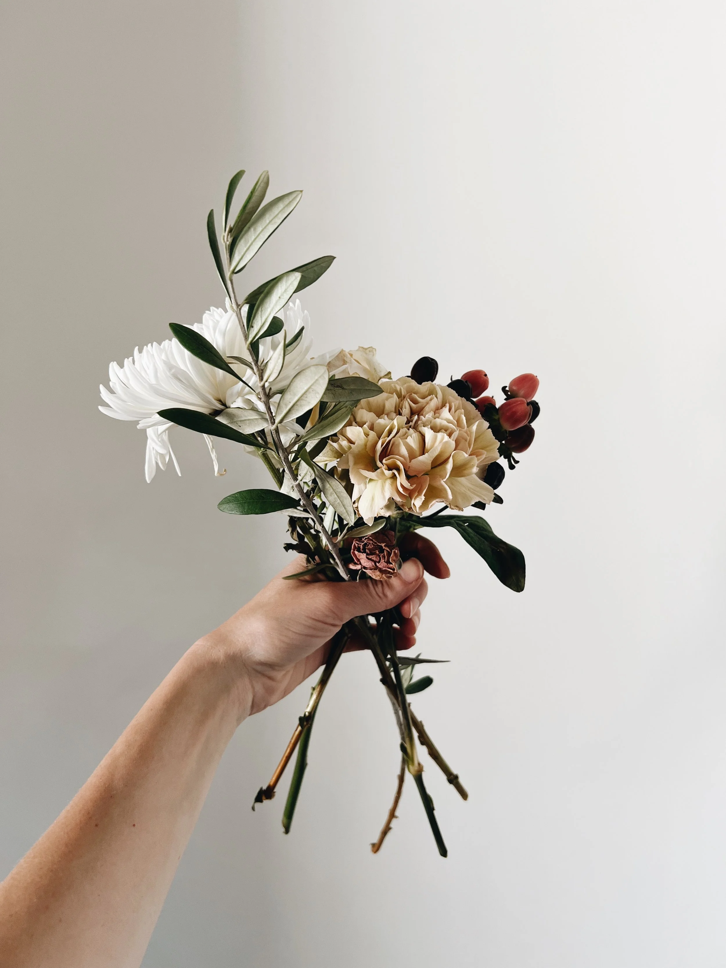 A hand holds gently a bouquet of foraged beauty, intimacy & Connective skills will guide you into relational capacity