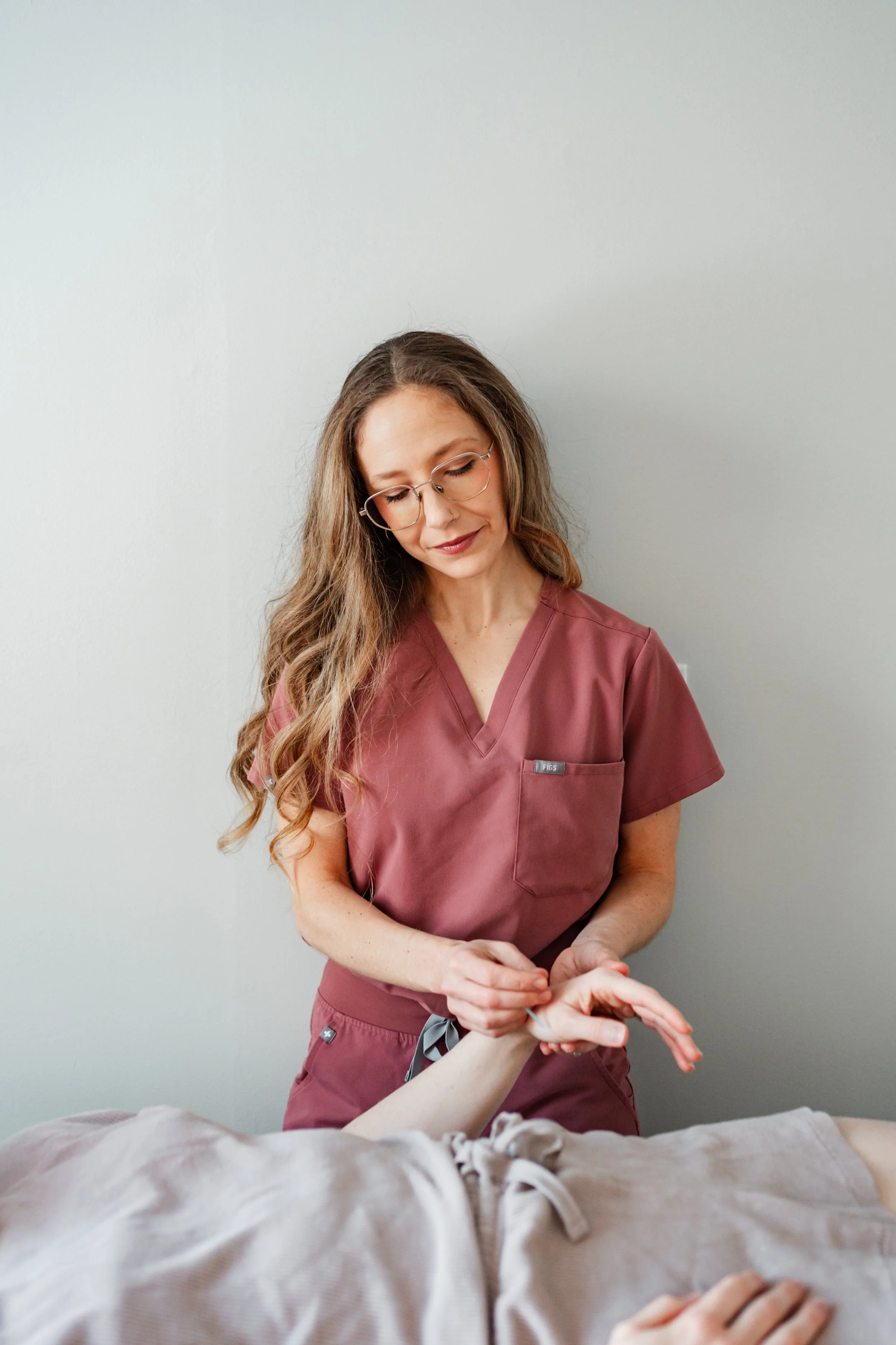 Female acupuncturist in pink scrubs smiling warmly, specializing in PCOS treatment at a Groton, MA wellness clinic