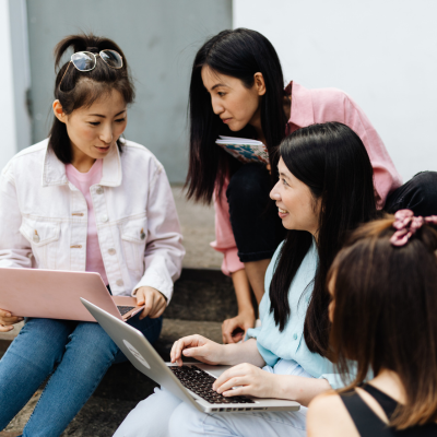 A group of fou students are seated and in an active discussion. Two of the students have their laptops open and are looking at each other.