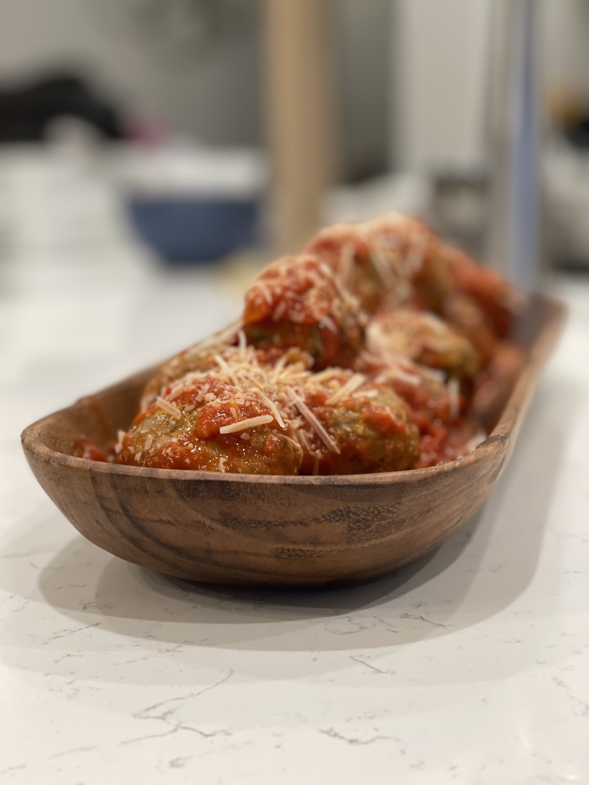 A wooden bowl with meatballs in tomato sauce topped with shredded cheese.