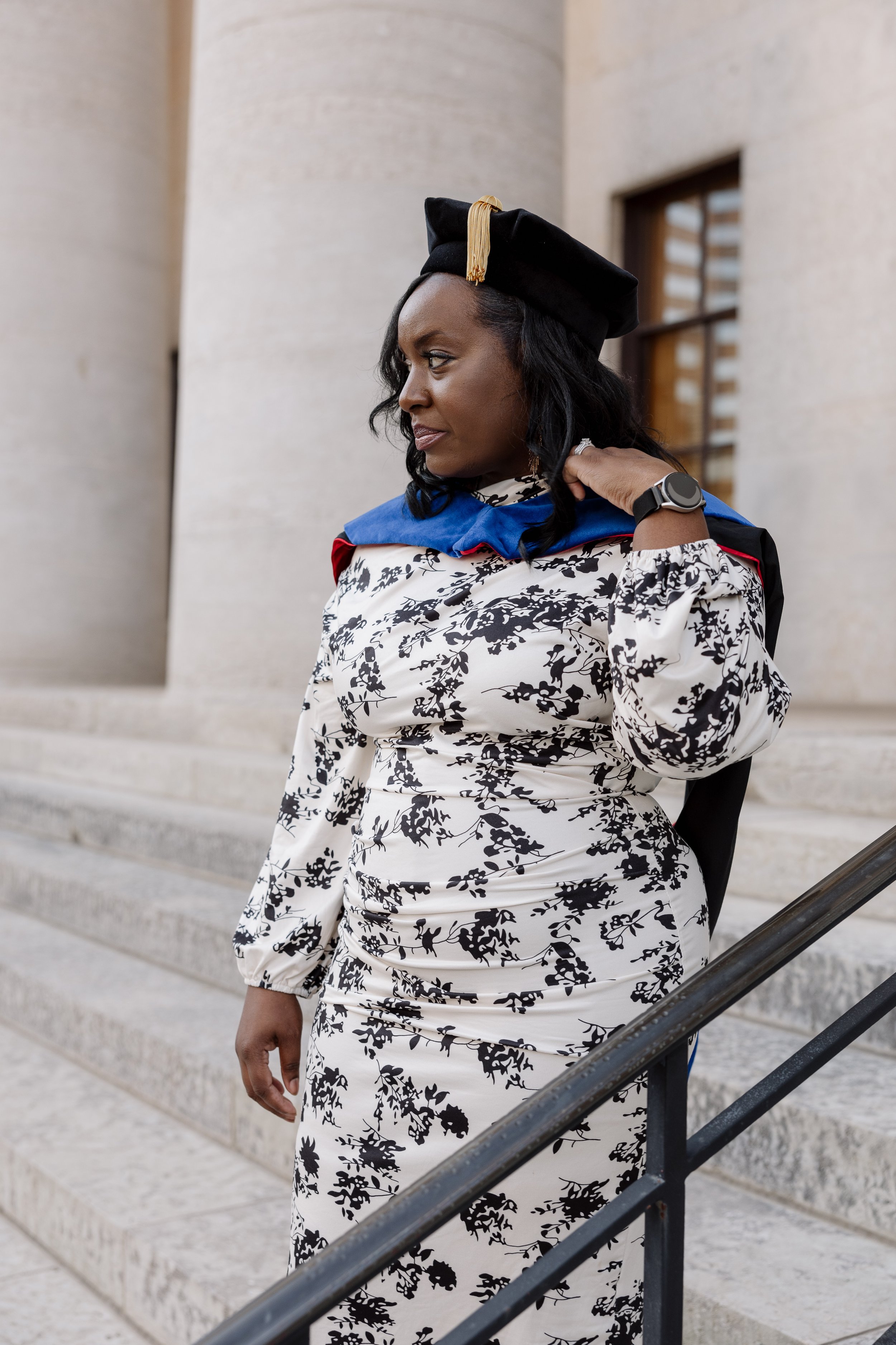 A woman in graduation cap and gown standing on steps outside a building.