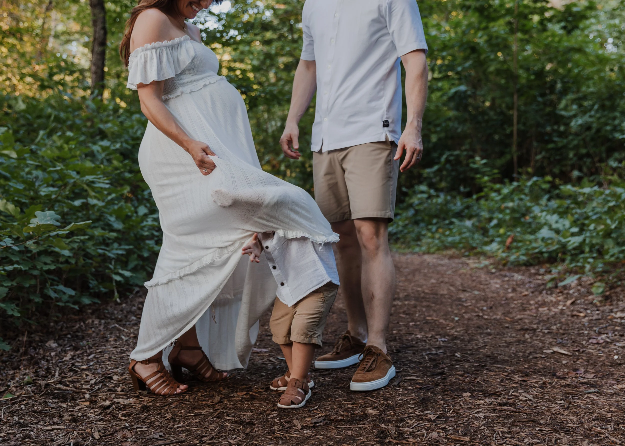 Two-year-old boy plays under mom's dress during a professional maternity photo session at Yates Mill in Raleigh, NC.