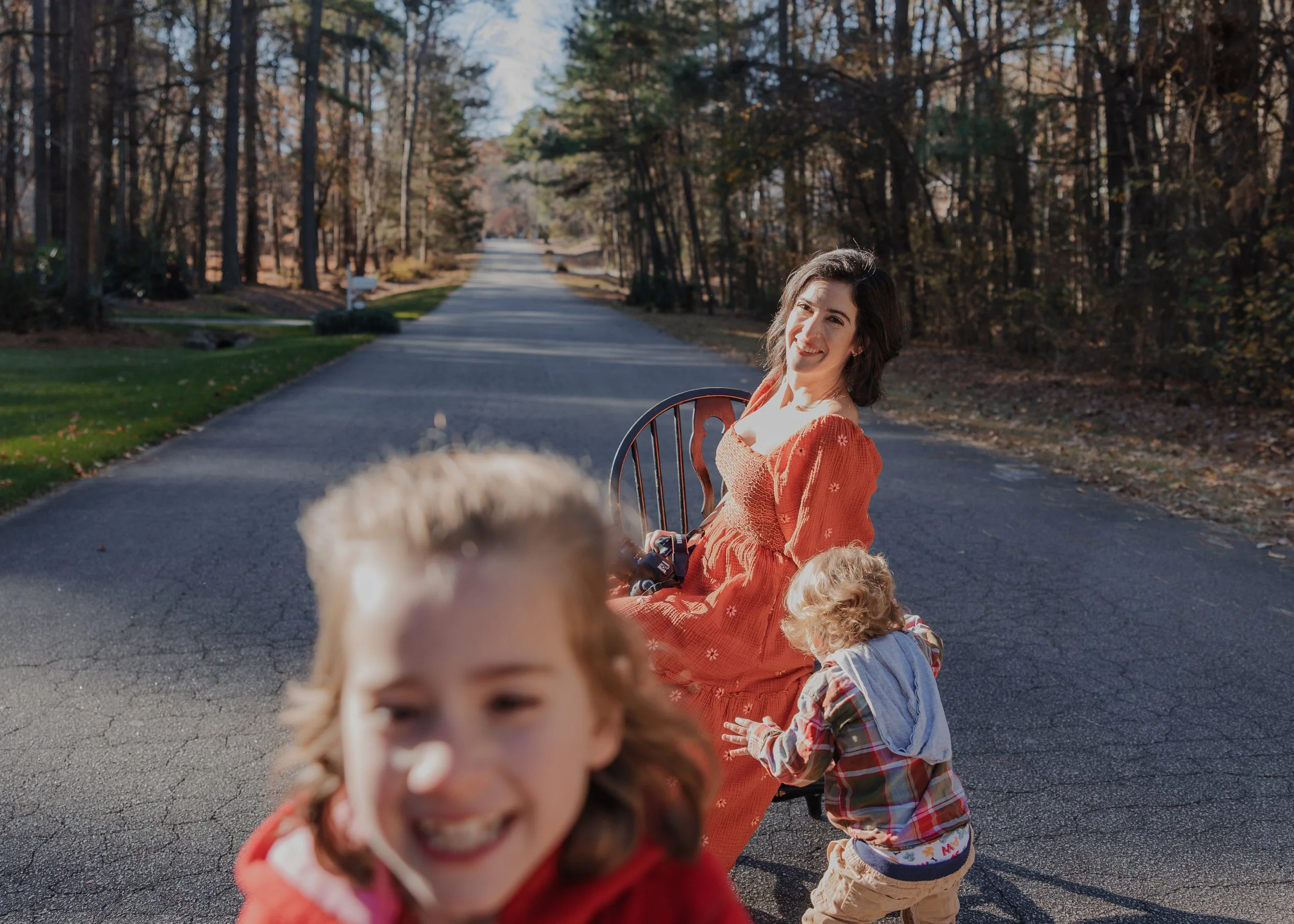 Photographer sits on chair while her kids run around her.