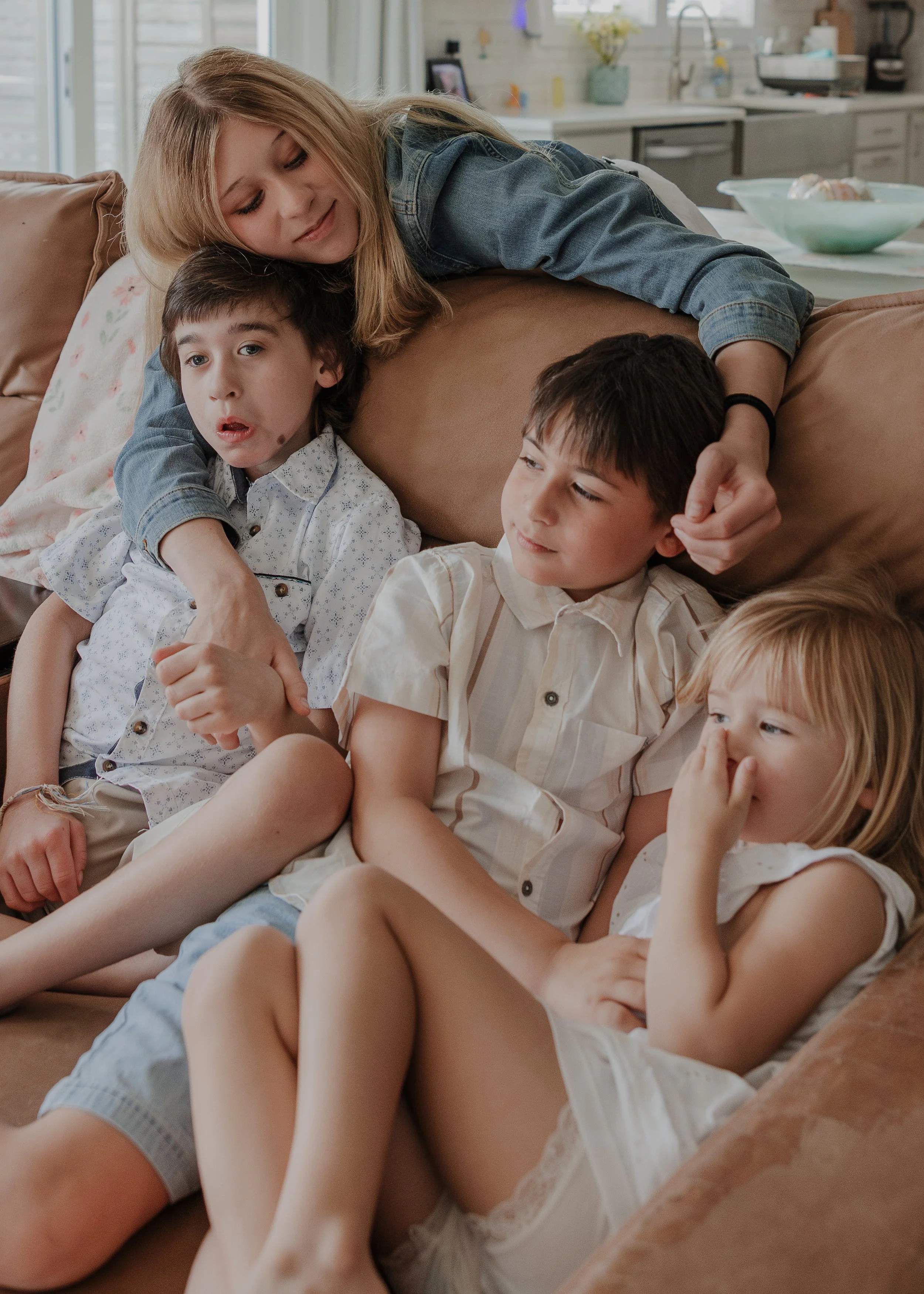 A candid moment of four siblings piled together on a leather sofa during an inclusive family session in Wendell, NC.