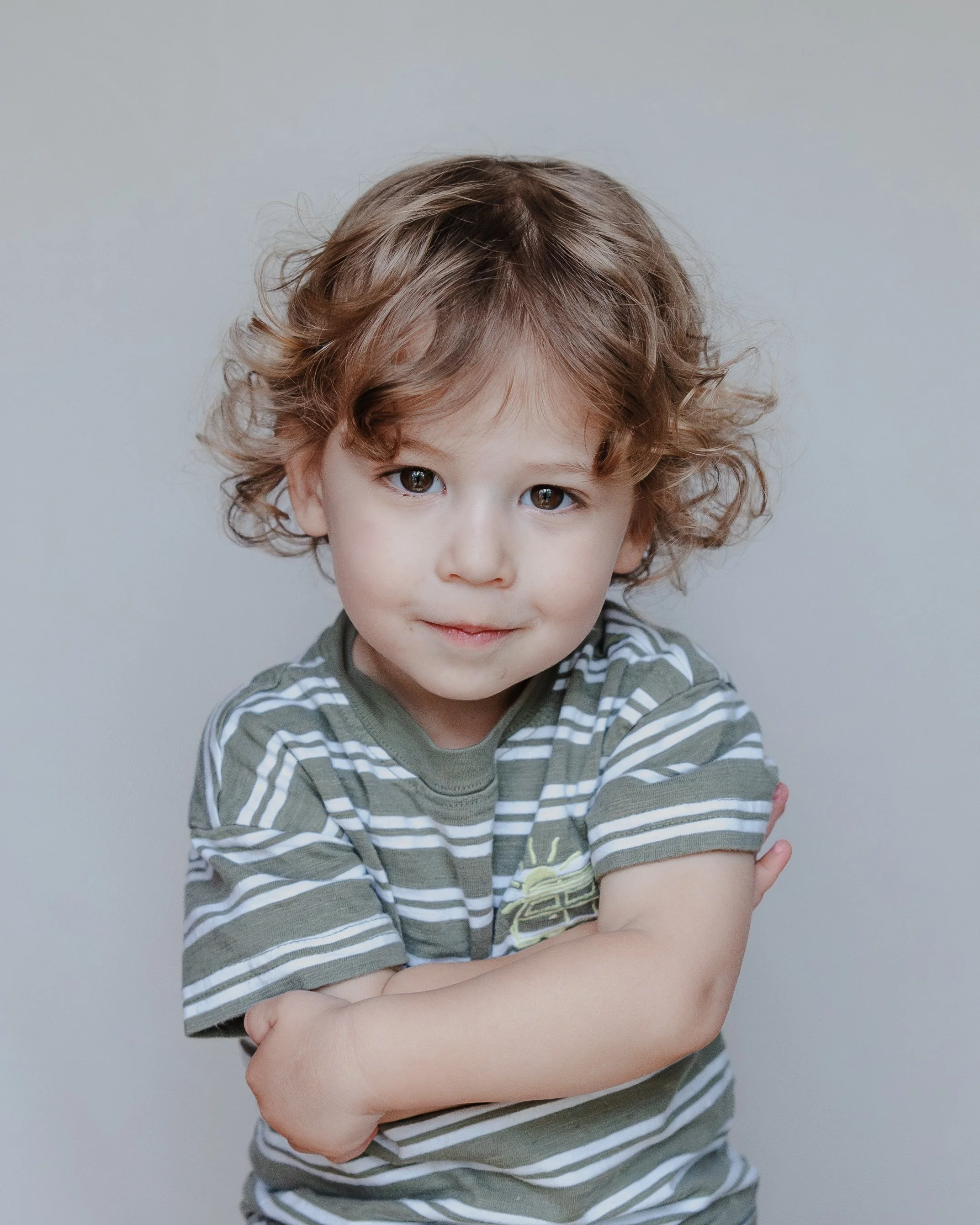A young boy in a striped shirt with curly hair looking directly at the camera with a soft smile during a modern school portrait session.