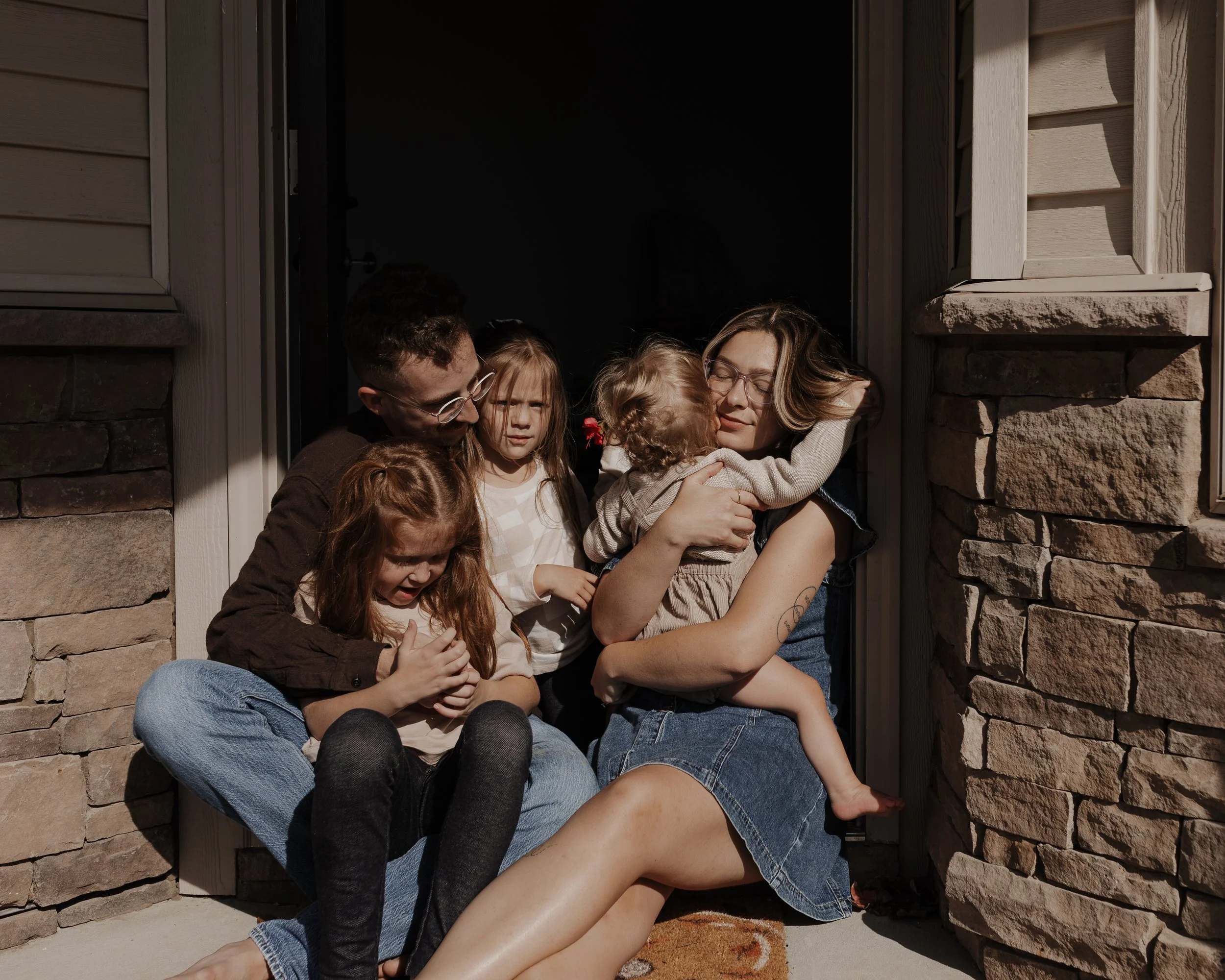 Family with three kids sit and hug in a doorway during an at-home family photo session in Knightdale, NC.