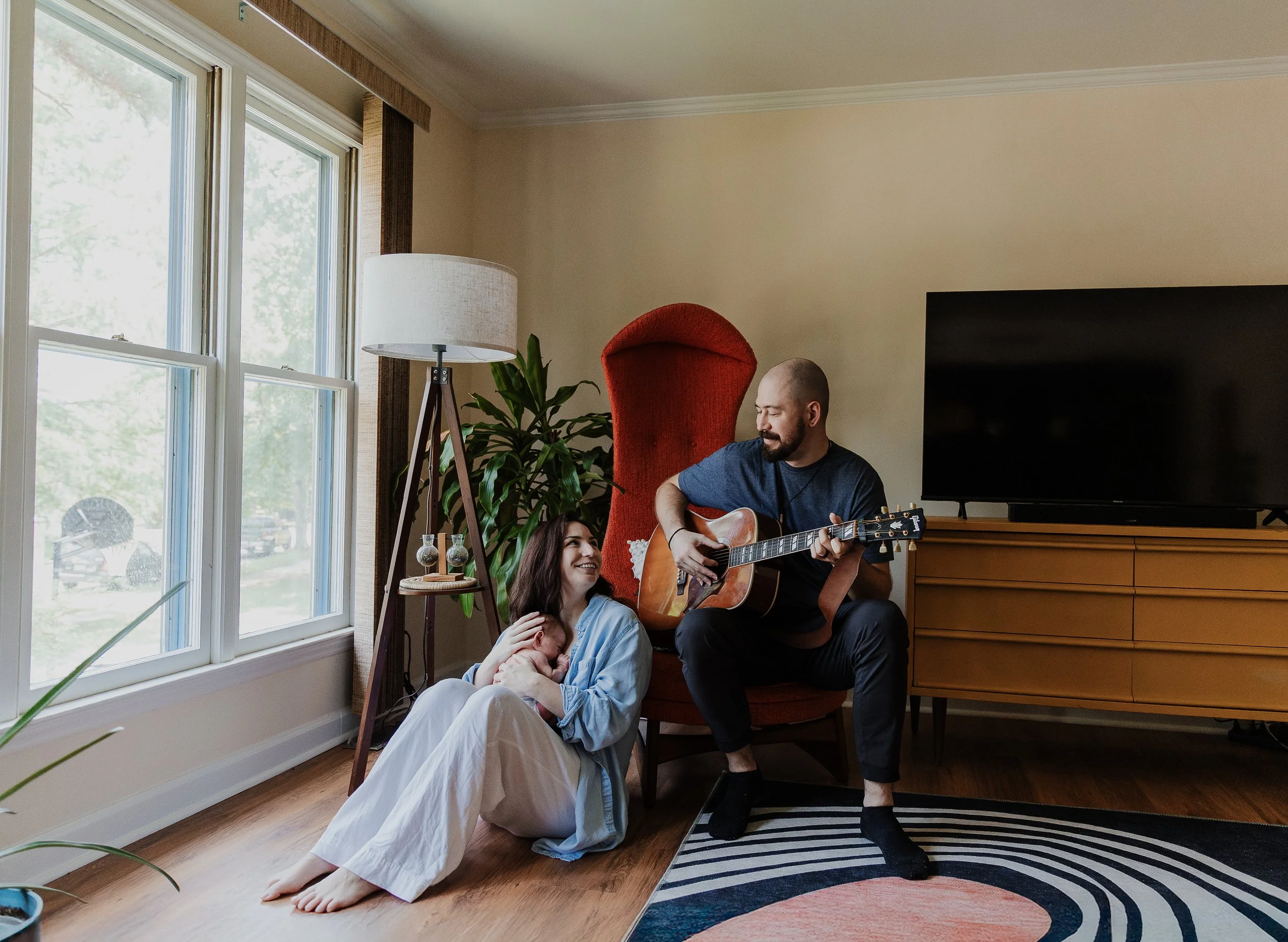 Relaxed newborn photos taken at home in Raleigh featuring parents and baby sitting and playing guitar.