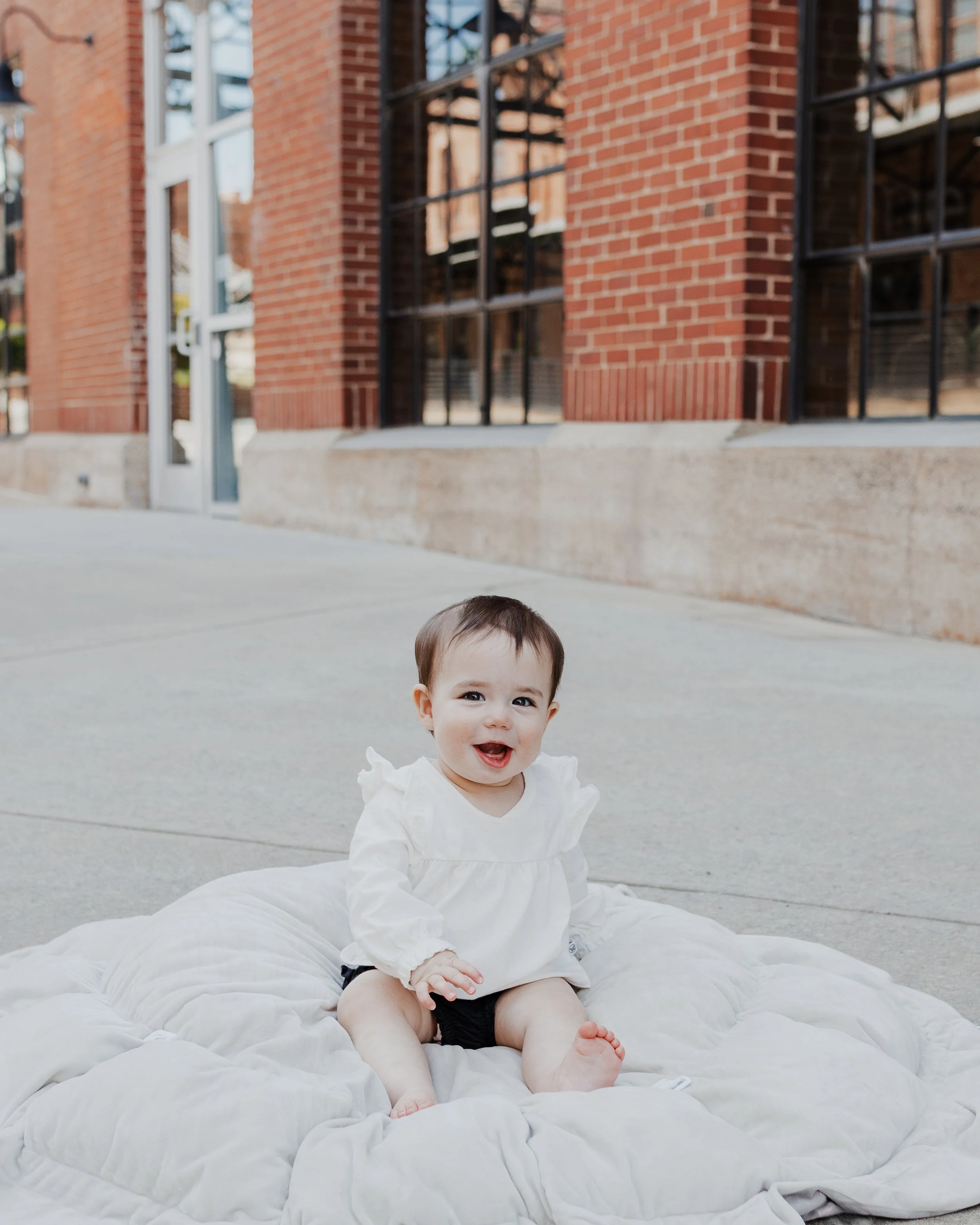 Baby sits and smiles on the sidewalk at American Tobacco Campus in Durham, NC.