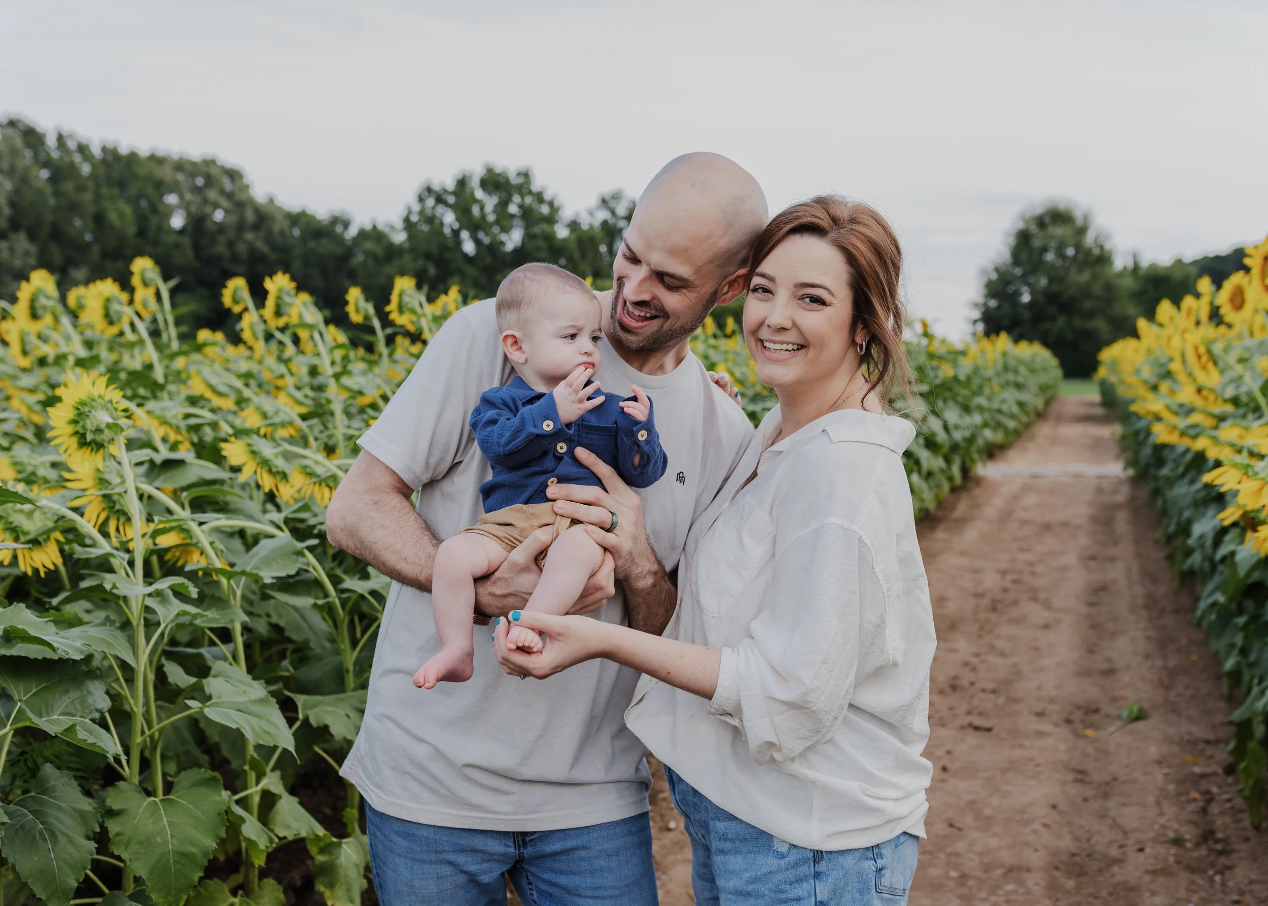 Young family holding their baby while standing in the sunflower fields at Dorothea Dix Park in Raleigh, North Carolina.