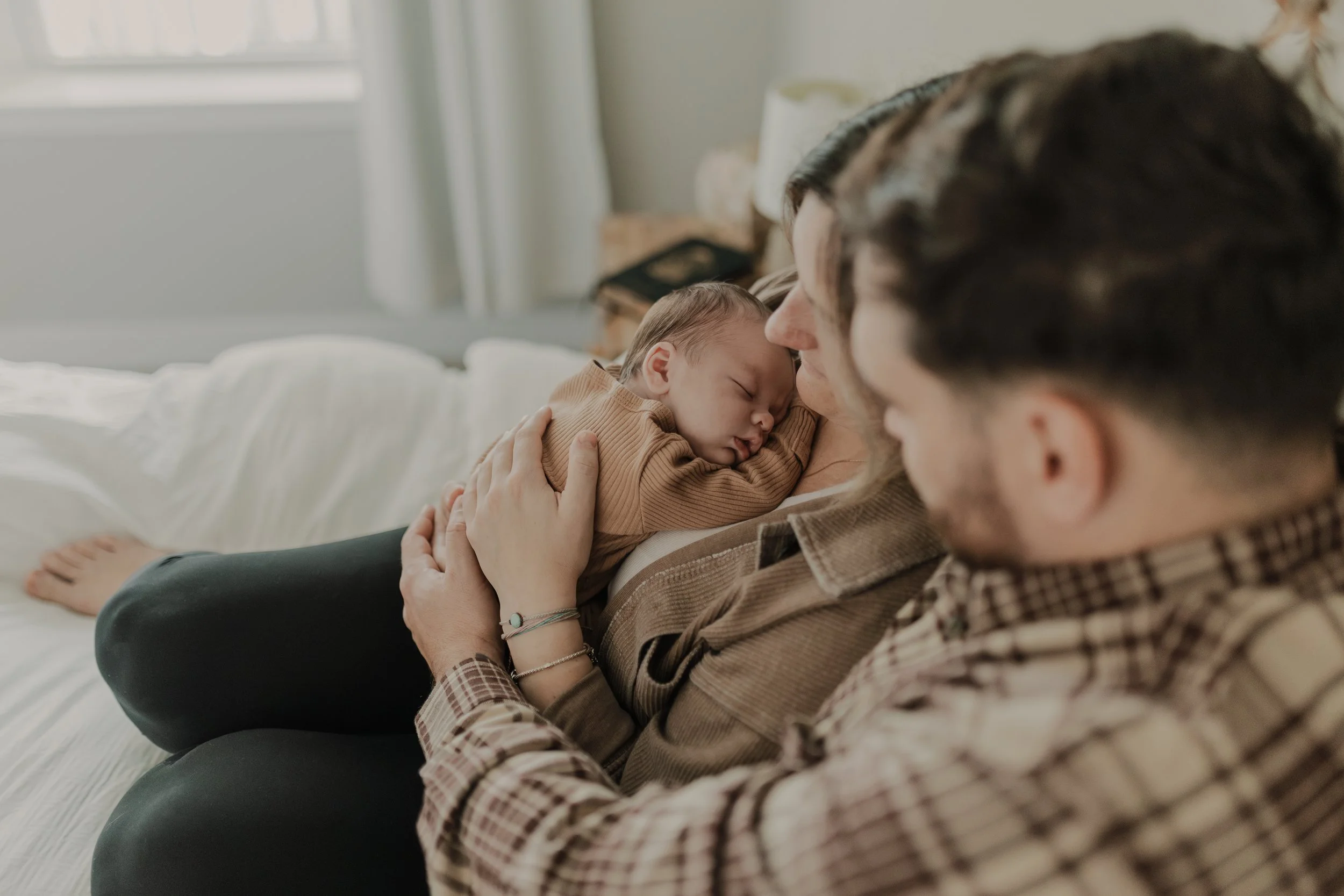 Mom and dad snuggle with baby on their bed while having newborn photos taken at home near Raleigh.
