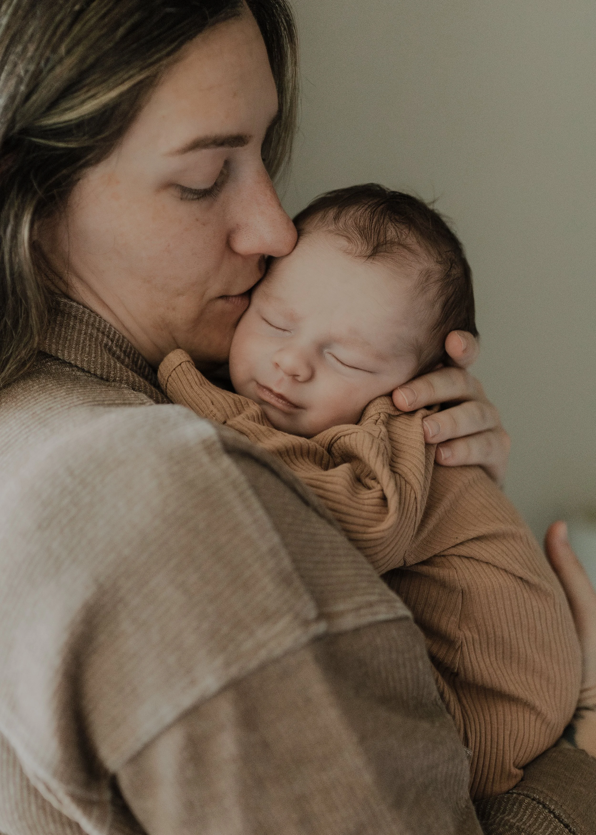 Mom kisses baby's cheek during a newborn lifestyle photo session at their apartment in Raleigh, NC.