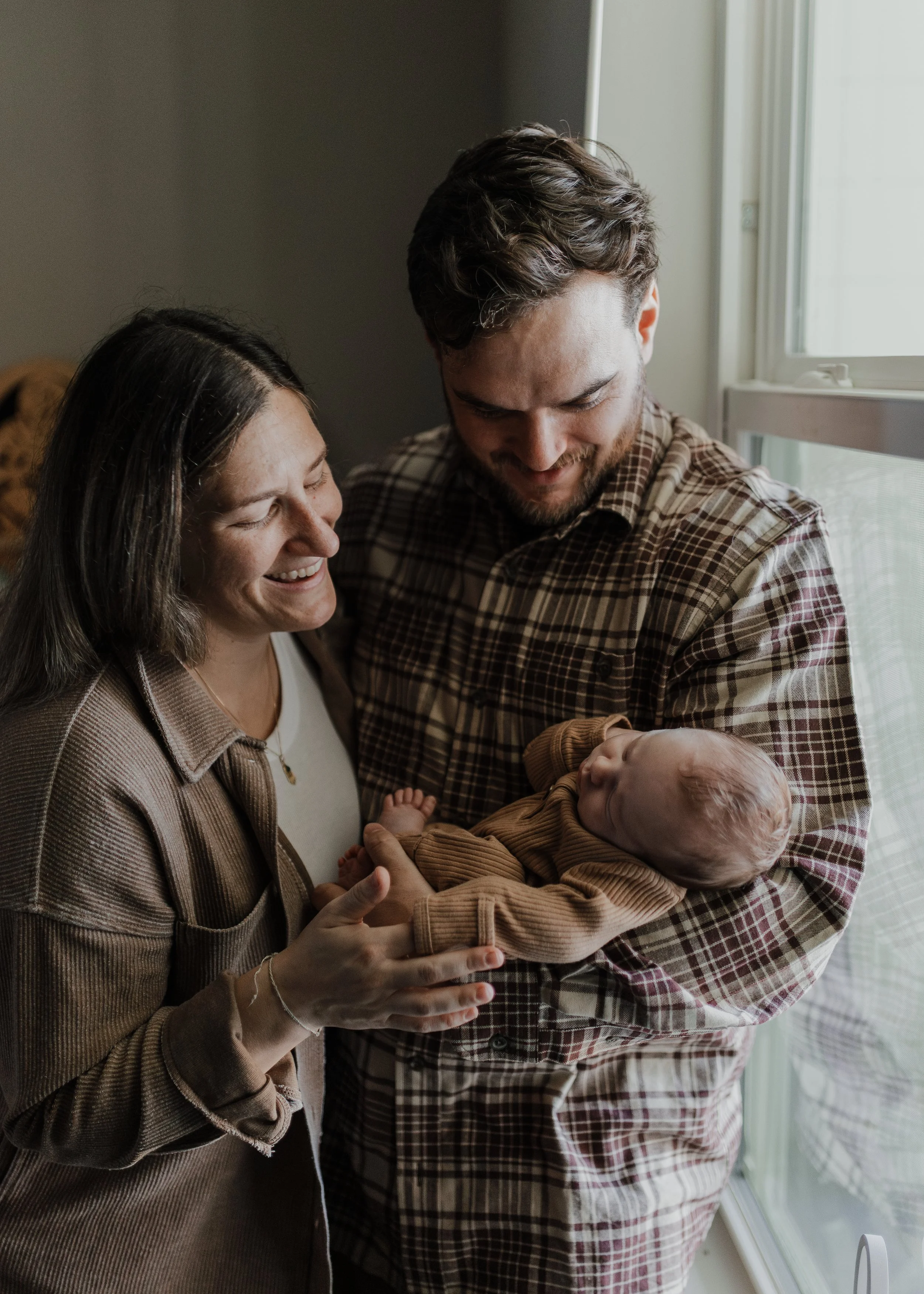 Mom and dad smile at their sleeping baby during professional newborn photos at home in Raleigh.