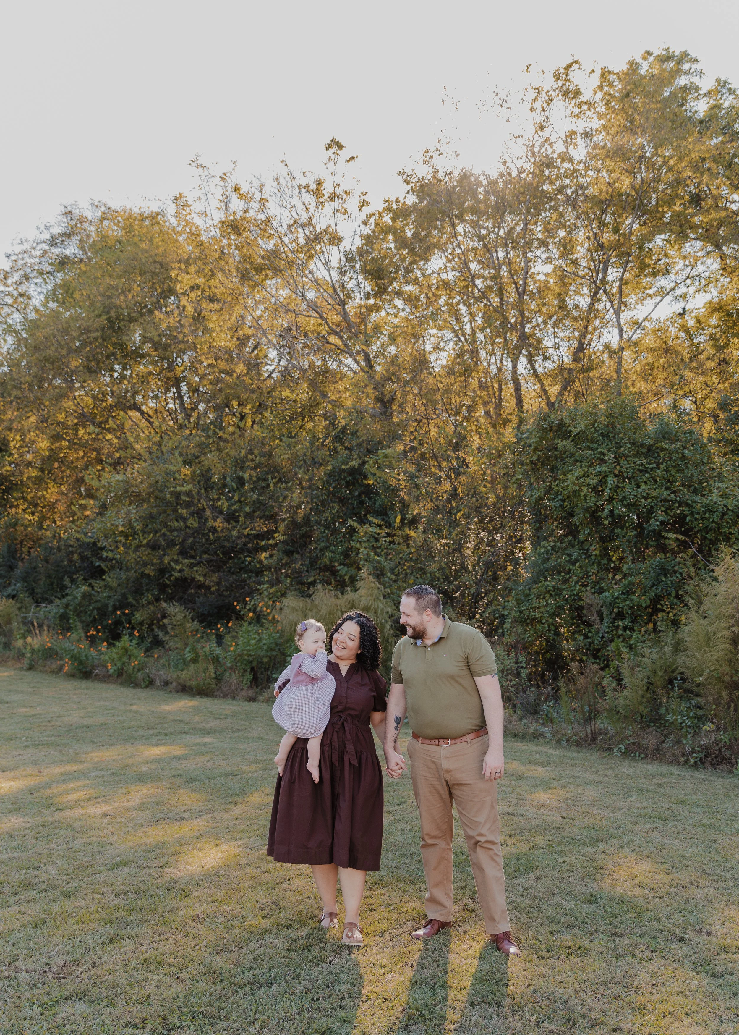 Mom, dad, and baby walk through a grassy field at Historic Oak View County Park during a professional fall family photography session.