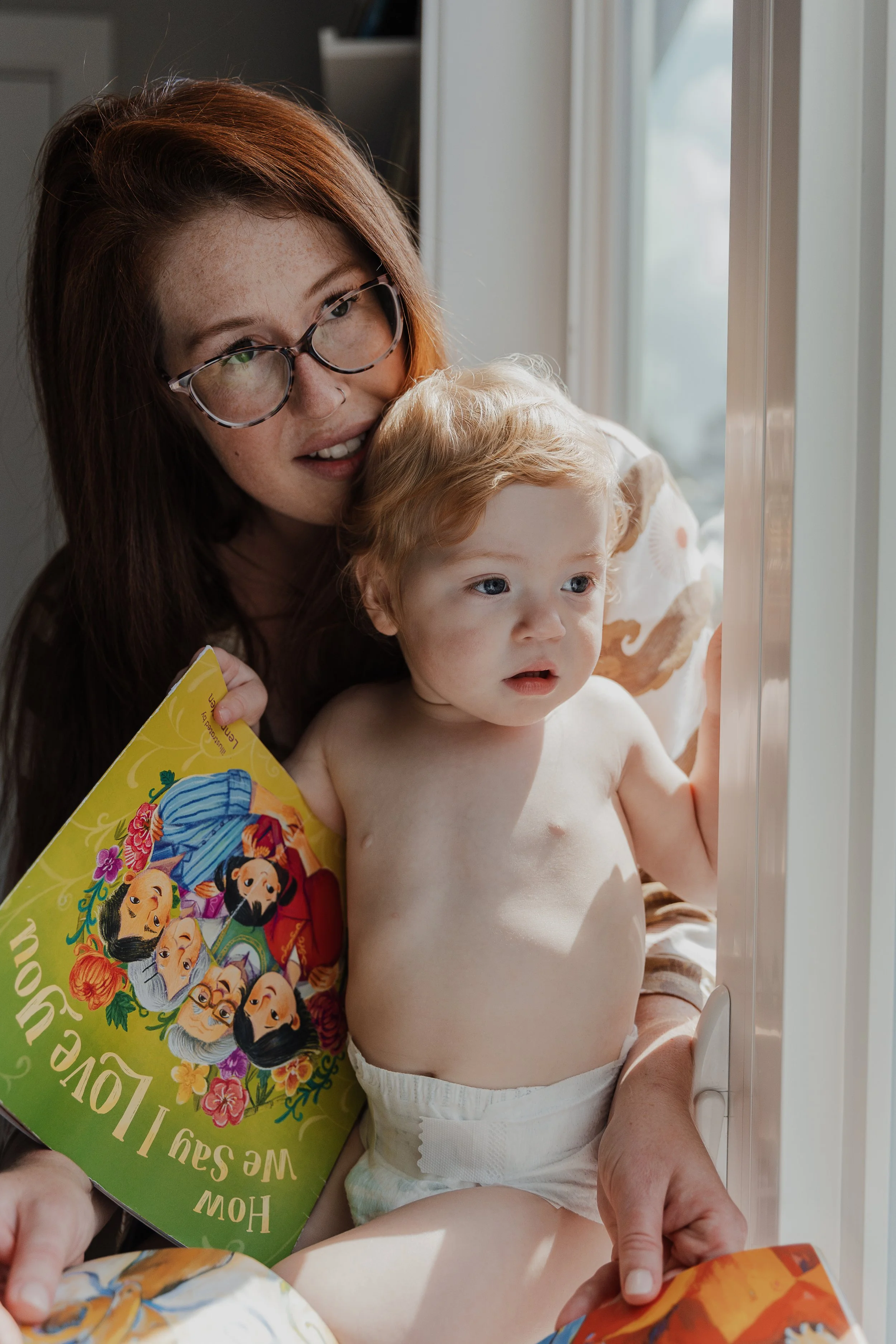 A mom and her toddler look out the window during a professional motherhood photography session in Raleigh.