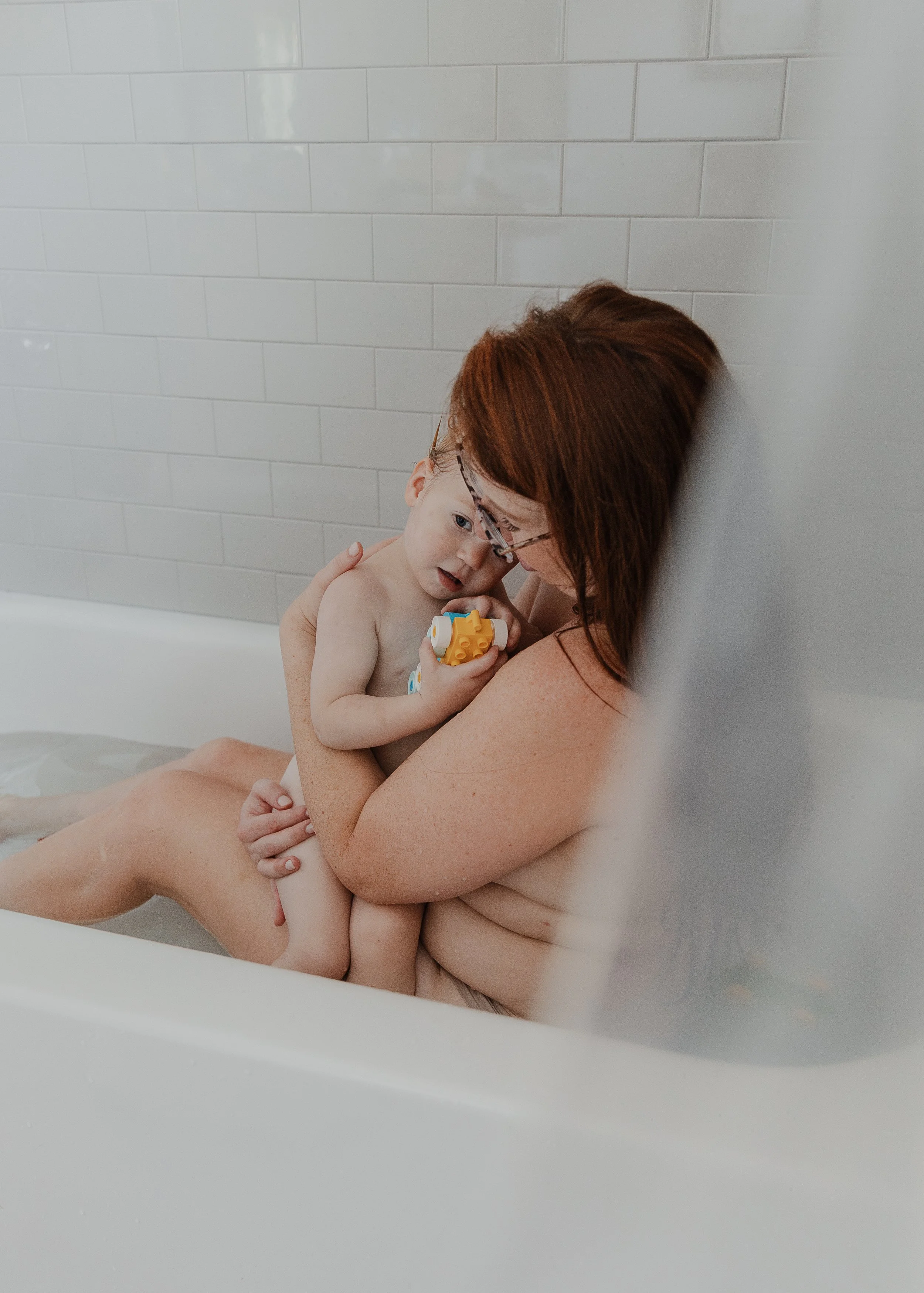 Mom hugs her toddler in the bath during a professional photoshoot celebrating motherhood in Raleigh, NC.