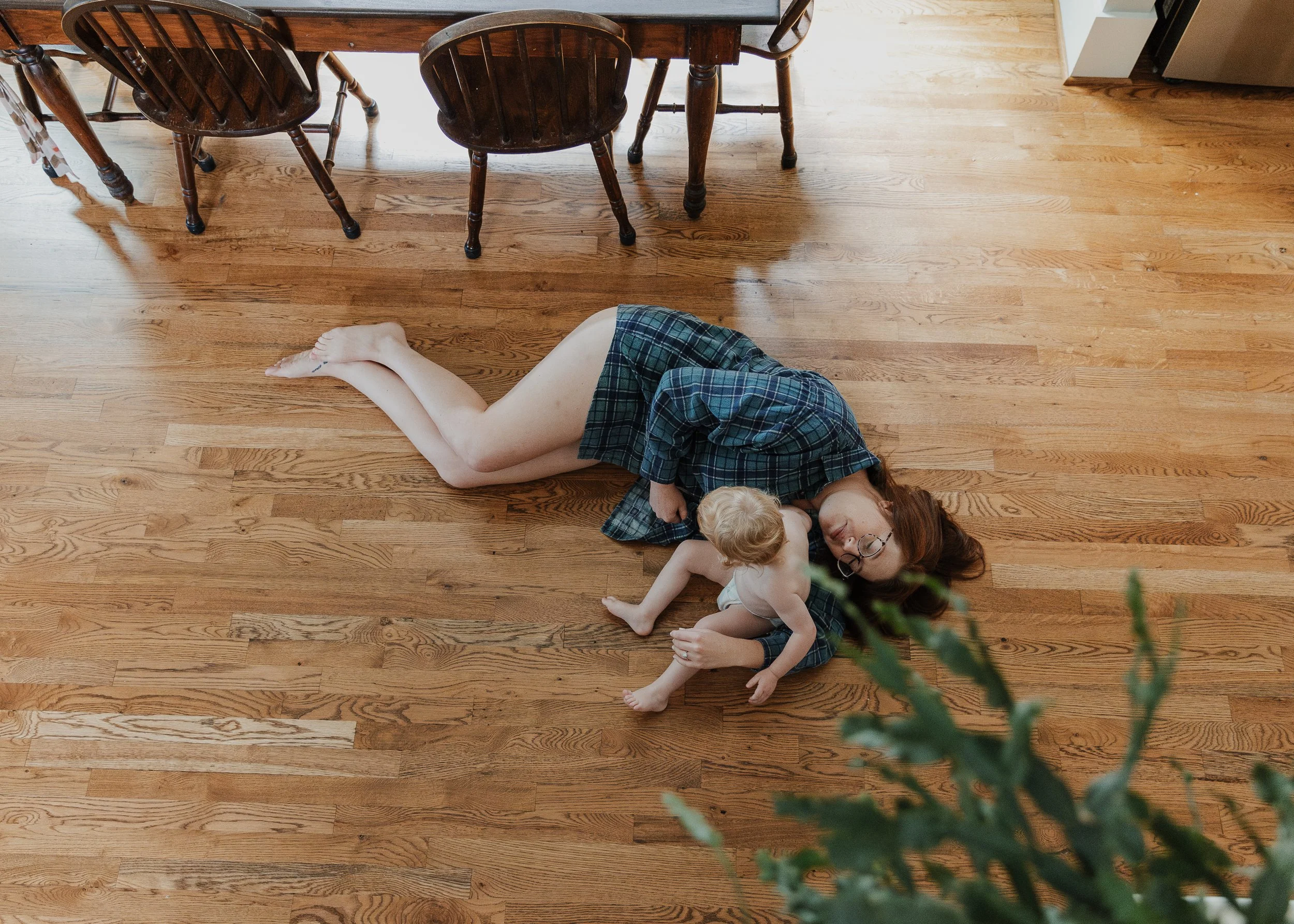 Mom lays on the floor with toddler to highlight the energy spent raising babies, captured during a professional photo session celebrating motherhood in Raleigh.