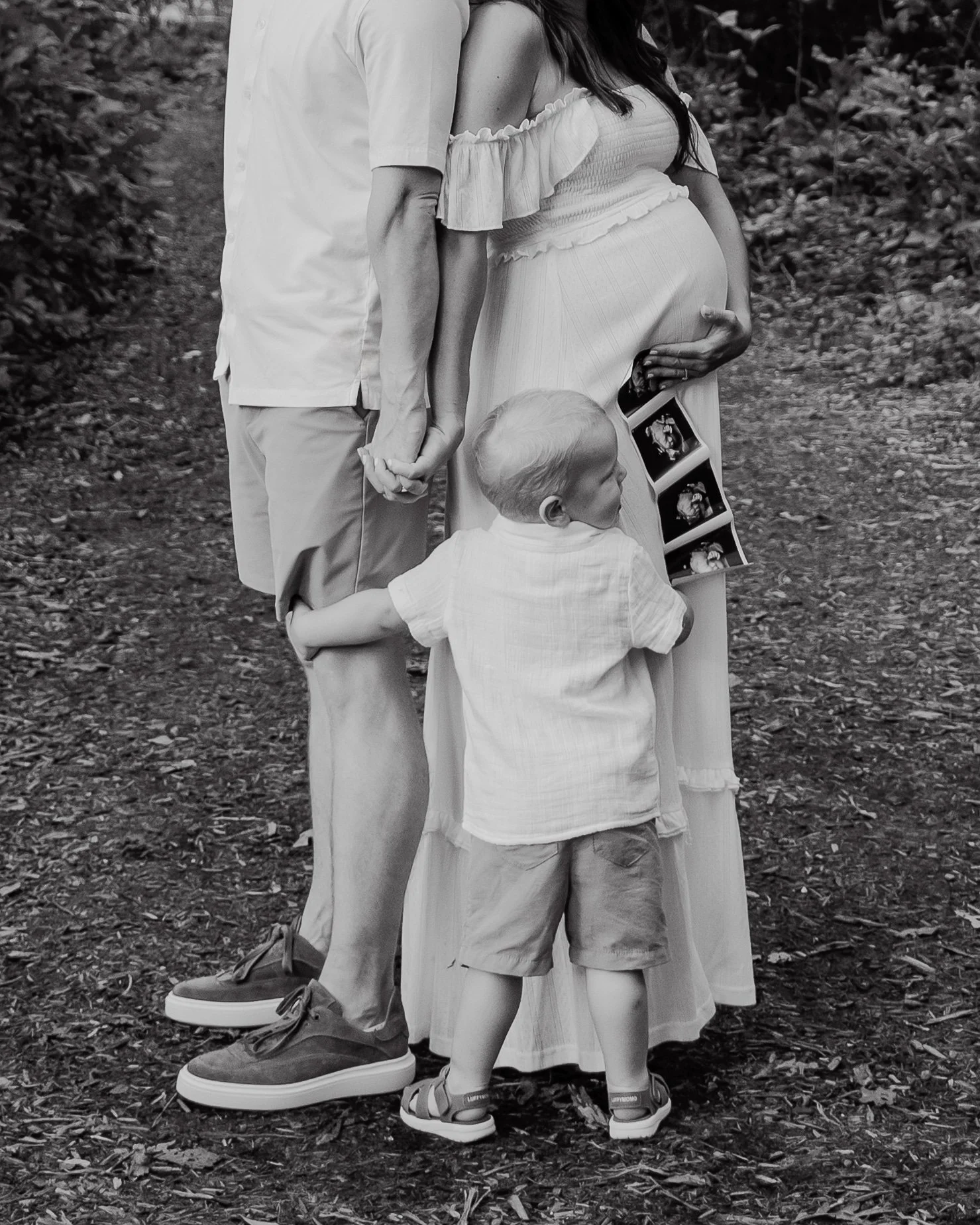 Black and white photo showing a pregnant woman and husband holding an ultrasound photo during a maternity photo session at Yates Mill County Park in Raleigh, NC.