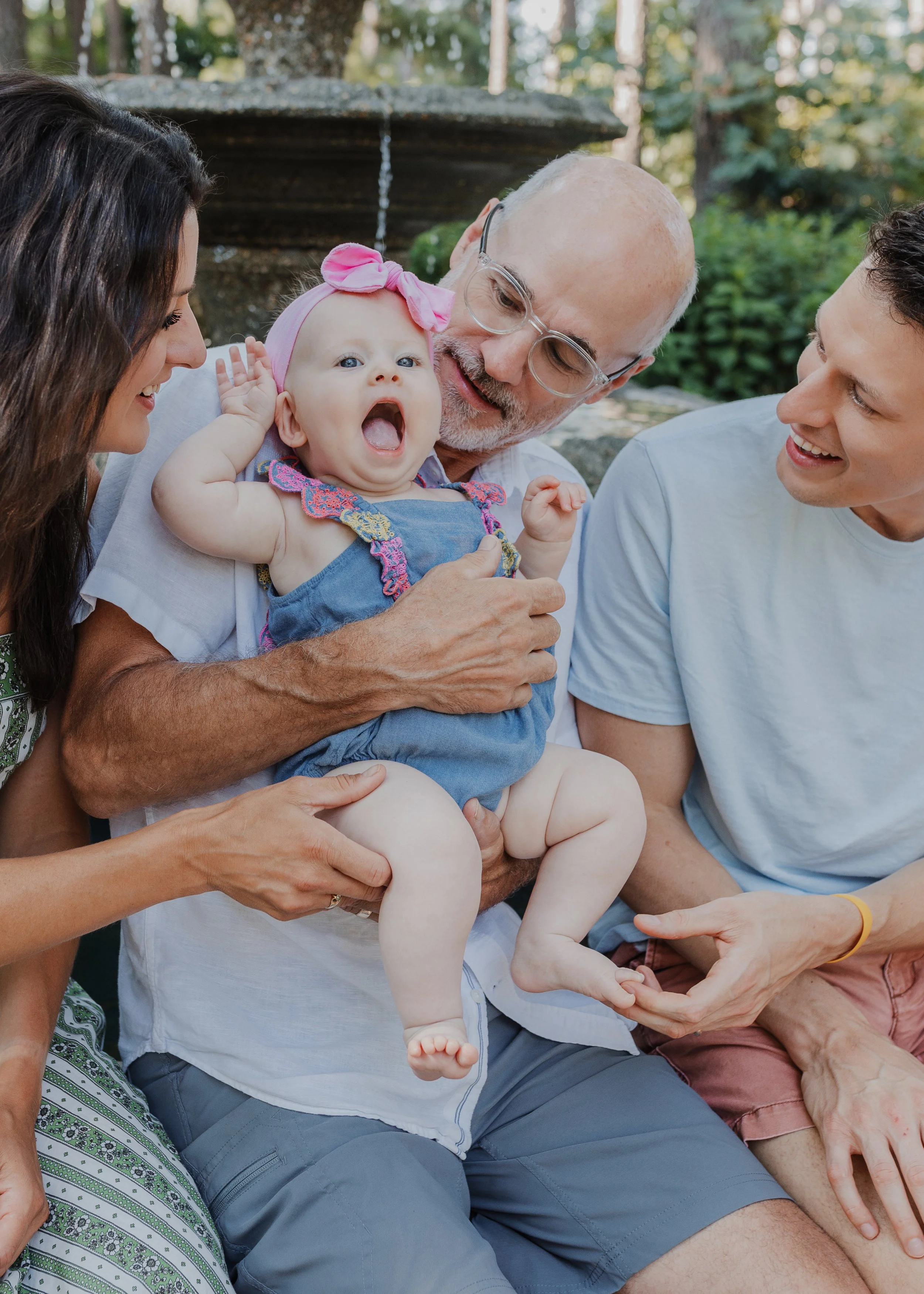 Grandfather holds grandaughter with family around during a spring family photo session at WRAL Azalea Gardens