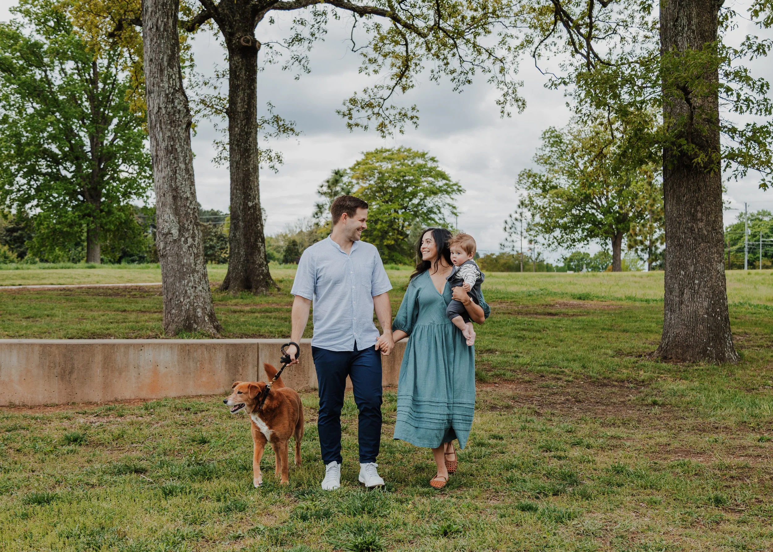 Family with dog and baby walk and laugh during a professional spring family photography shoot at NCMA in Raleigh, NC.