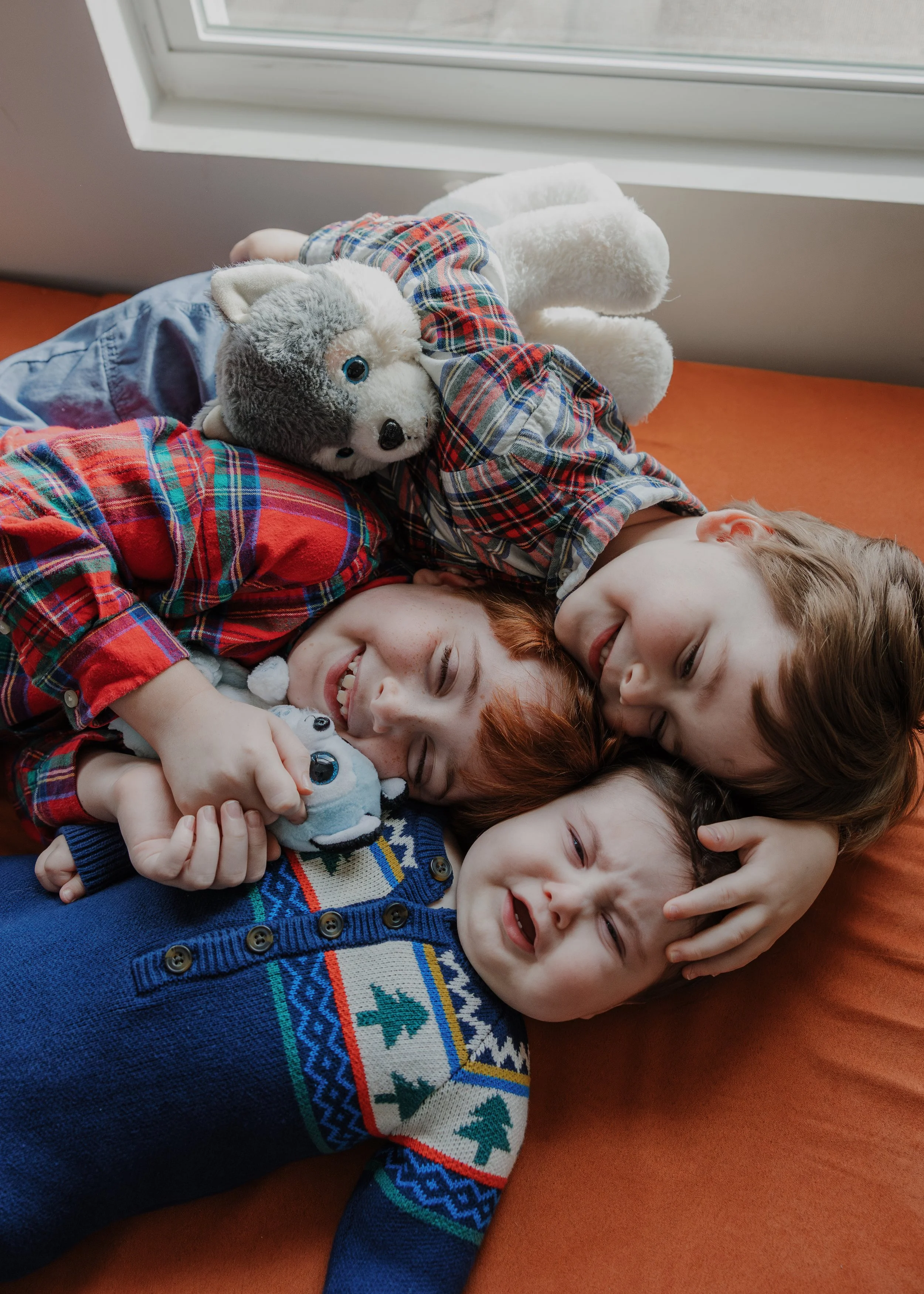 3 brothers cuddle and laugh on their nugget during a professional family photo session at home in North Carolina.